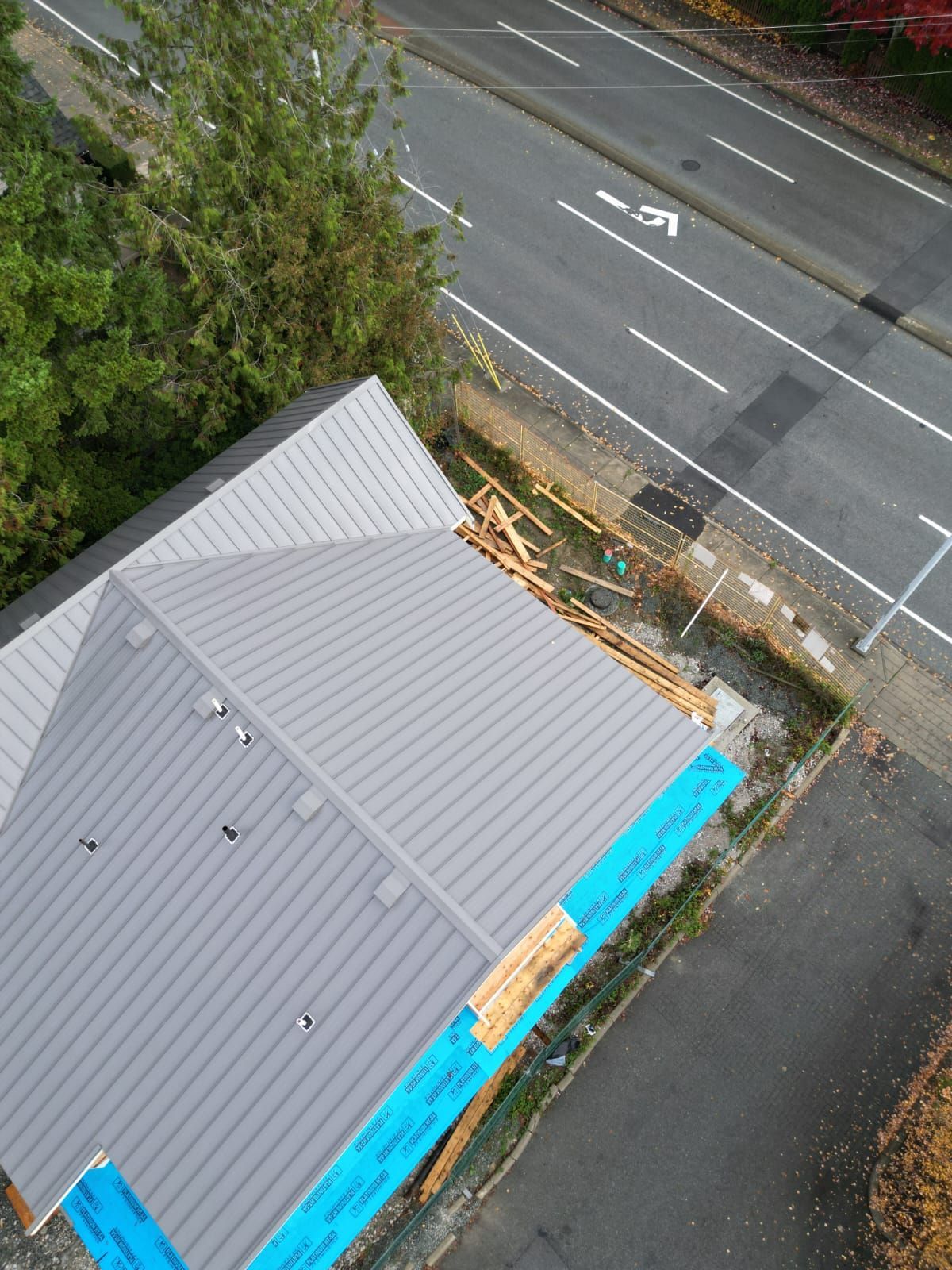 An aerial view of a building under construction, featuring a finished gray metal roof and blue protective exterior wraps.