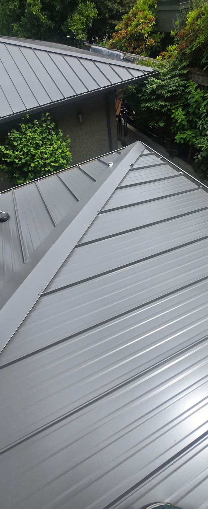 Standing seam metal roof with a hip cap and a second metal roof beside a stucco wall