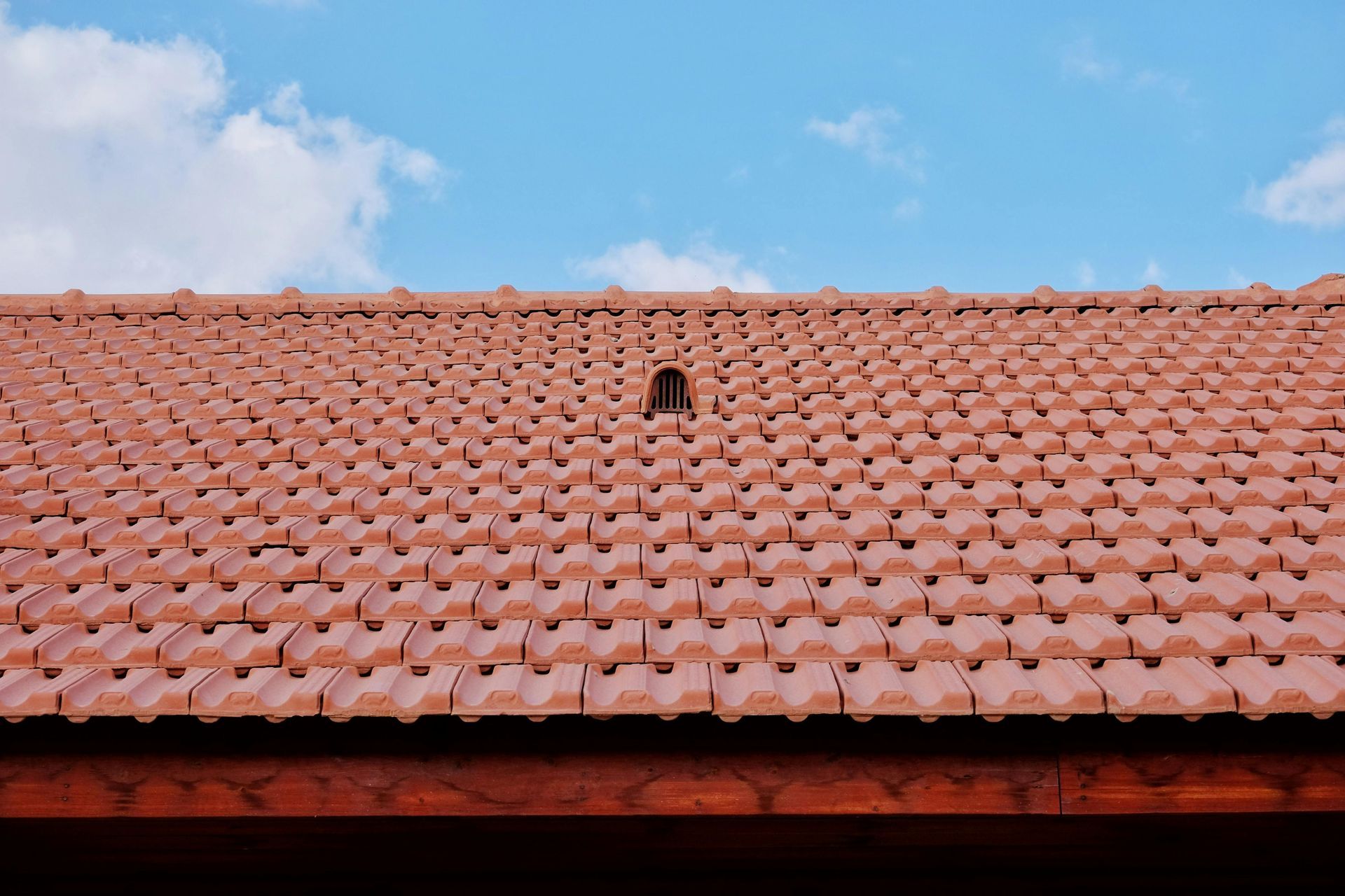 A roof with a vent on it and a building in the background.