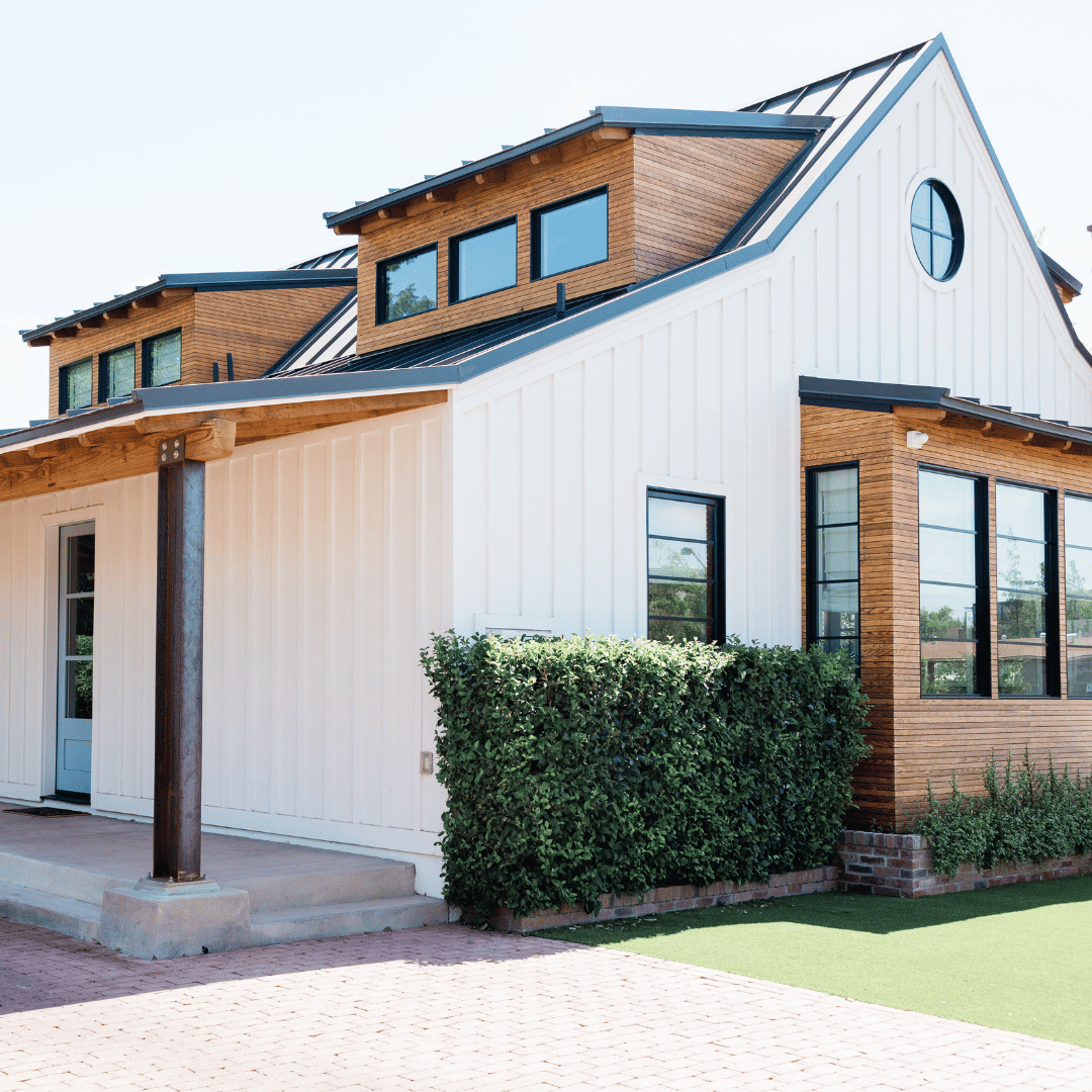 A modern house with white board-and-batten siding, wood accents, black window frames, and a circular gable window.