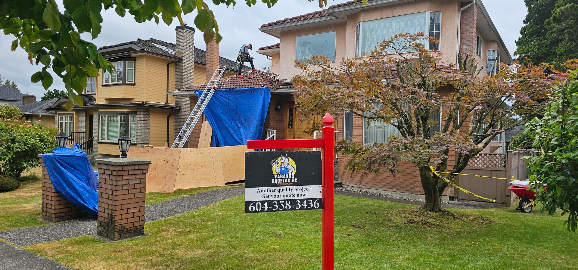 A residential home under construction with a blue tarp on the roof, scaffolding, and a construction company sign.