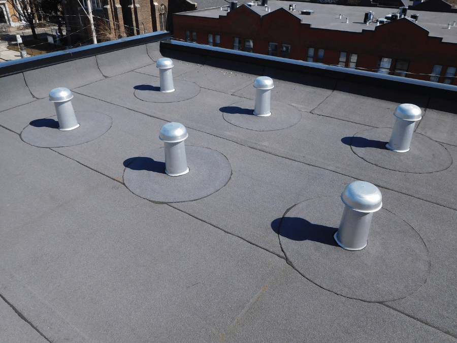 A roof with a vent on it and a building in the background.