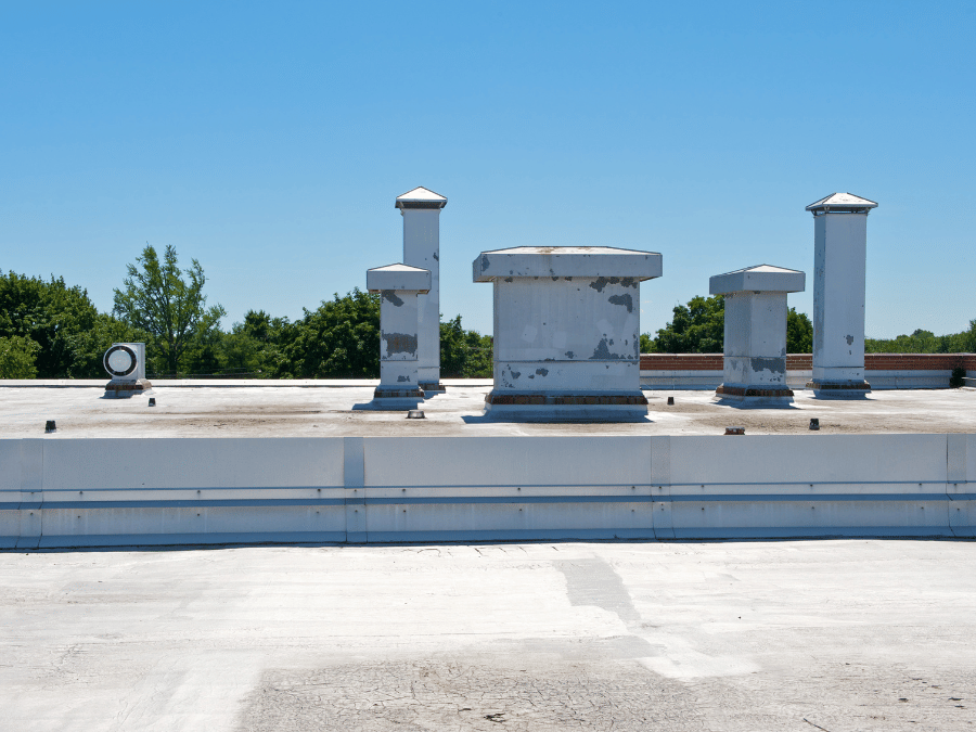 A roof with a vent on it and a building in the background.
