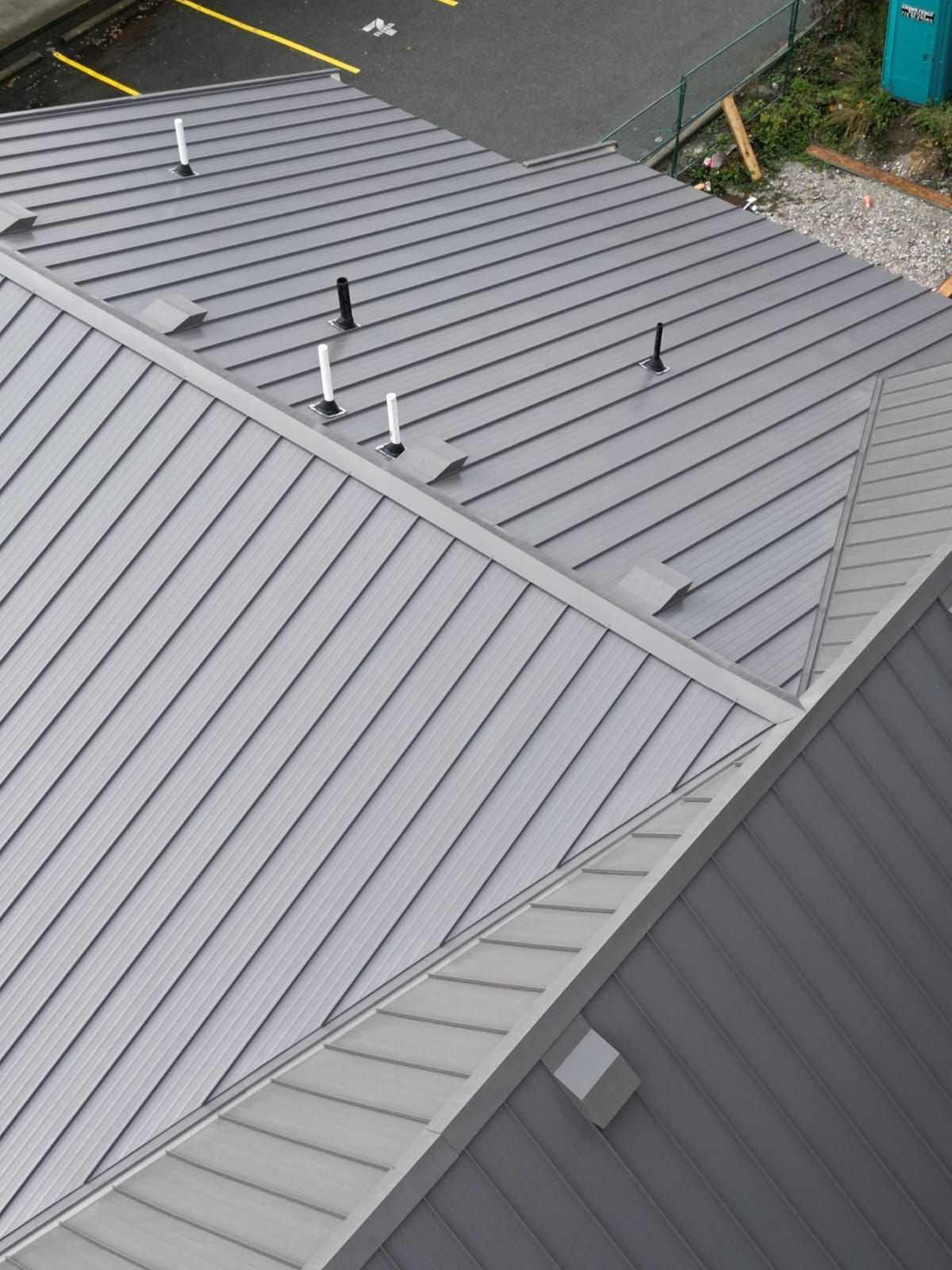 An elevated view of a gray, metal-paneled roof with several vents and plumbing pipes extending from its surface.