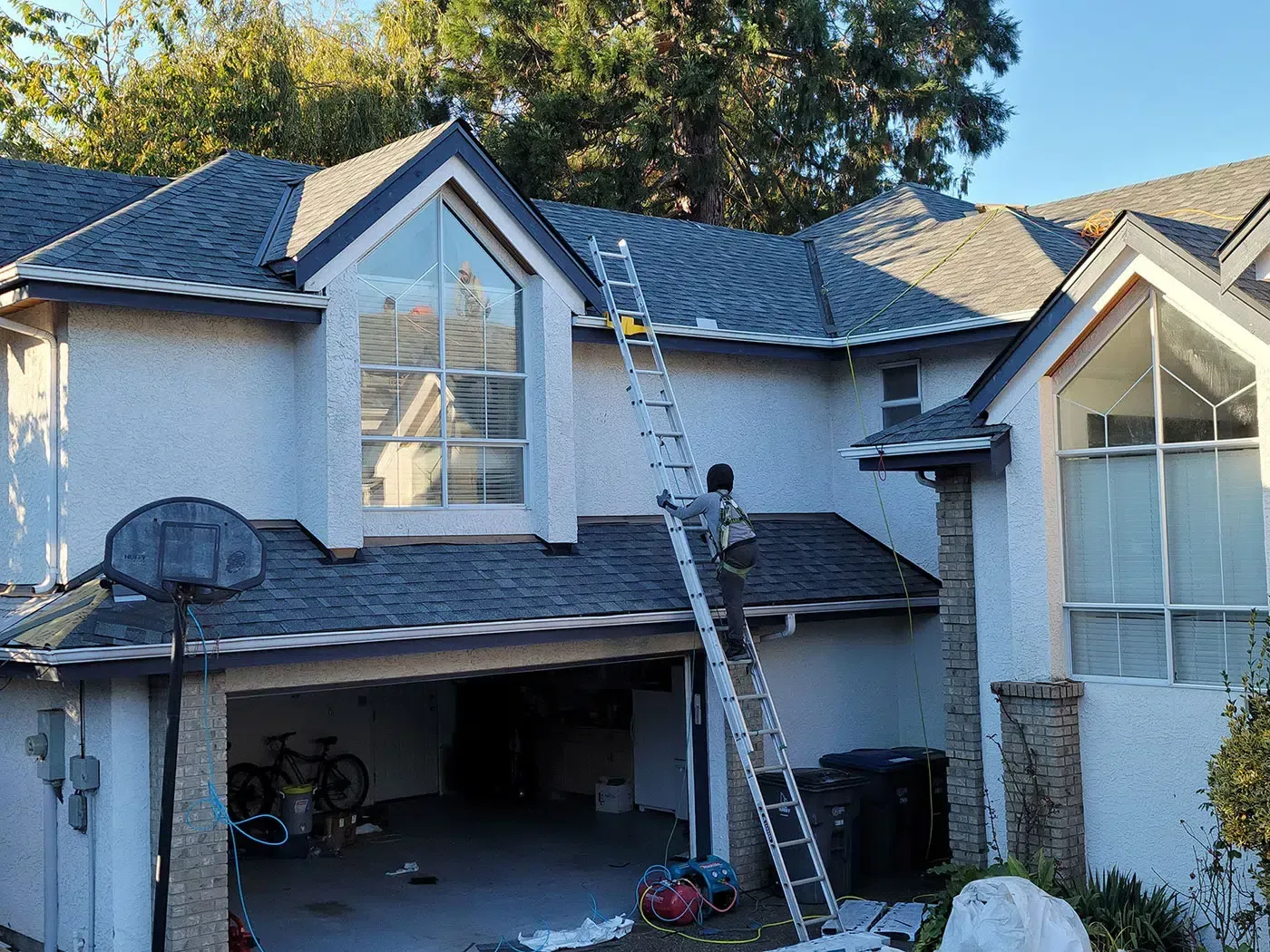 A person climbs an extension ladder leaned against the light-colored exterior wall of a two-story home.