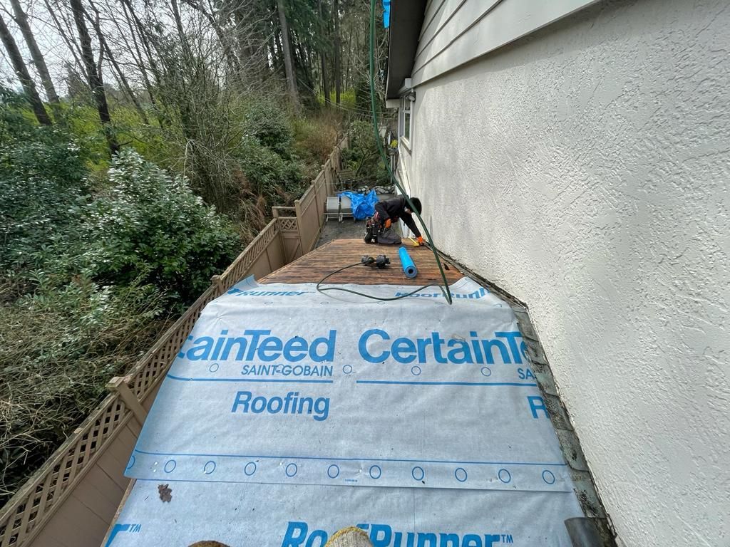 A man is laying roofing paper on the side of a house.