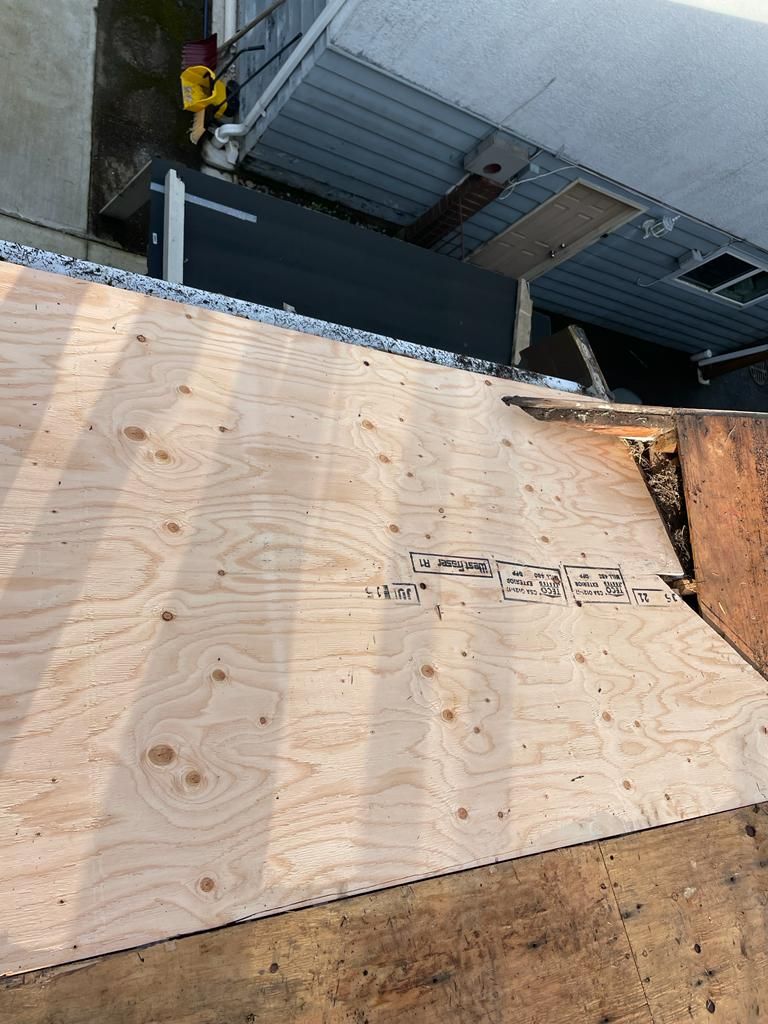 A piece of plywood decking is installed on top of a roof next to a house.