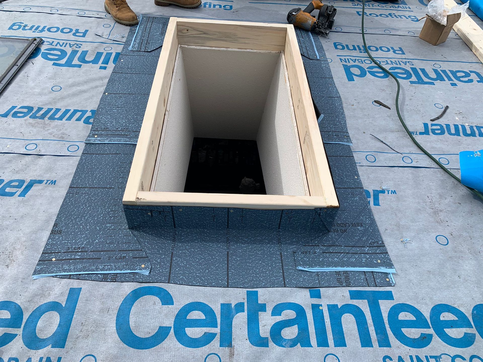 Rectangular roof vent opening framed in beige on blue CertainTeed underlayment on a flat roof
