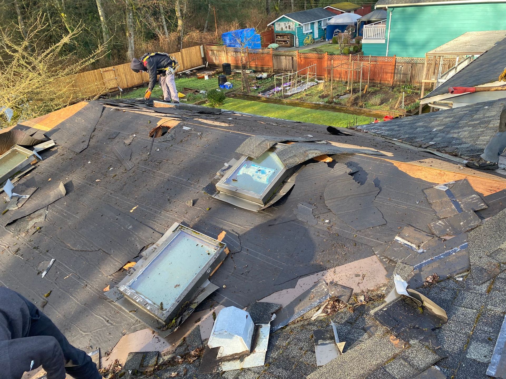 A roof with a lot of pieces of asphalt shingles, underlay material, and skylights on it.
