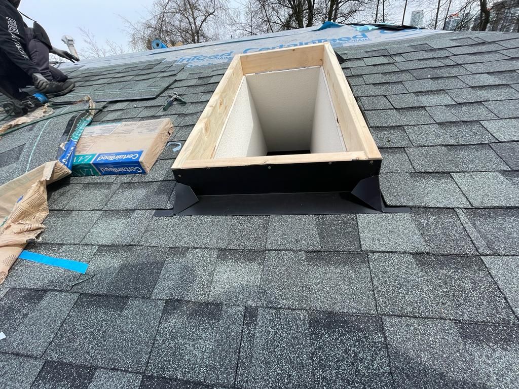 A skylight frame installed on a shingled roof, with tools and materials nearby during construction.