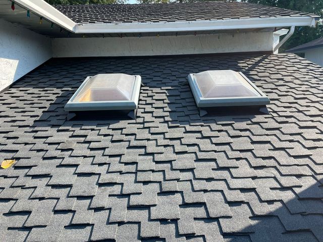 Two dome skylights on dark textured roofing beneath an upper roof eave