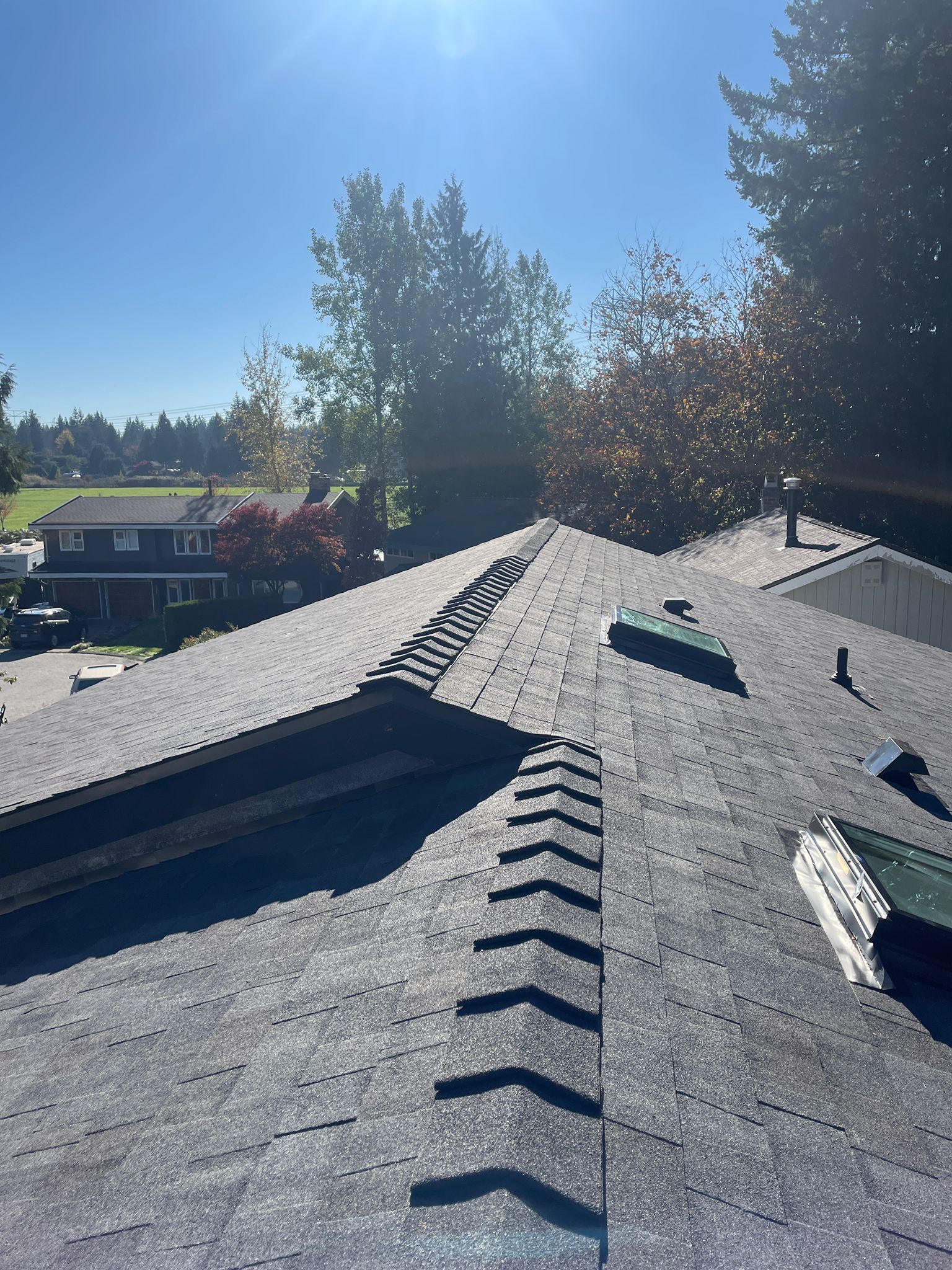 A view from above looking down the angled peaks of a gray shingled roof under a bright, sunny sky.