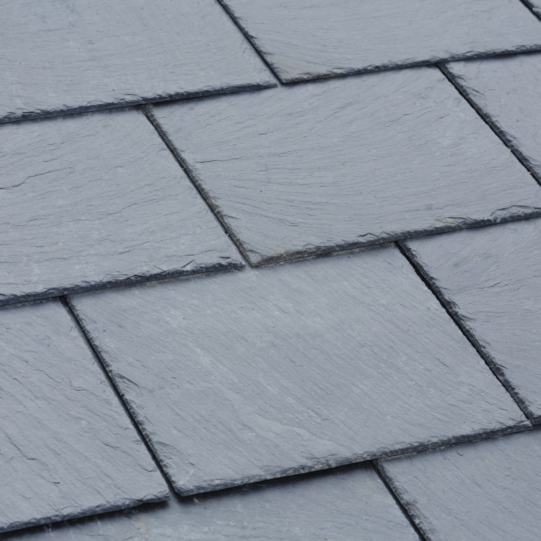 A close-up view of overlapping grey, textured rectangular roofing slate tiles laid in a standard pattern.