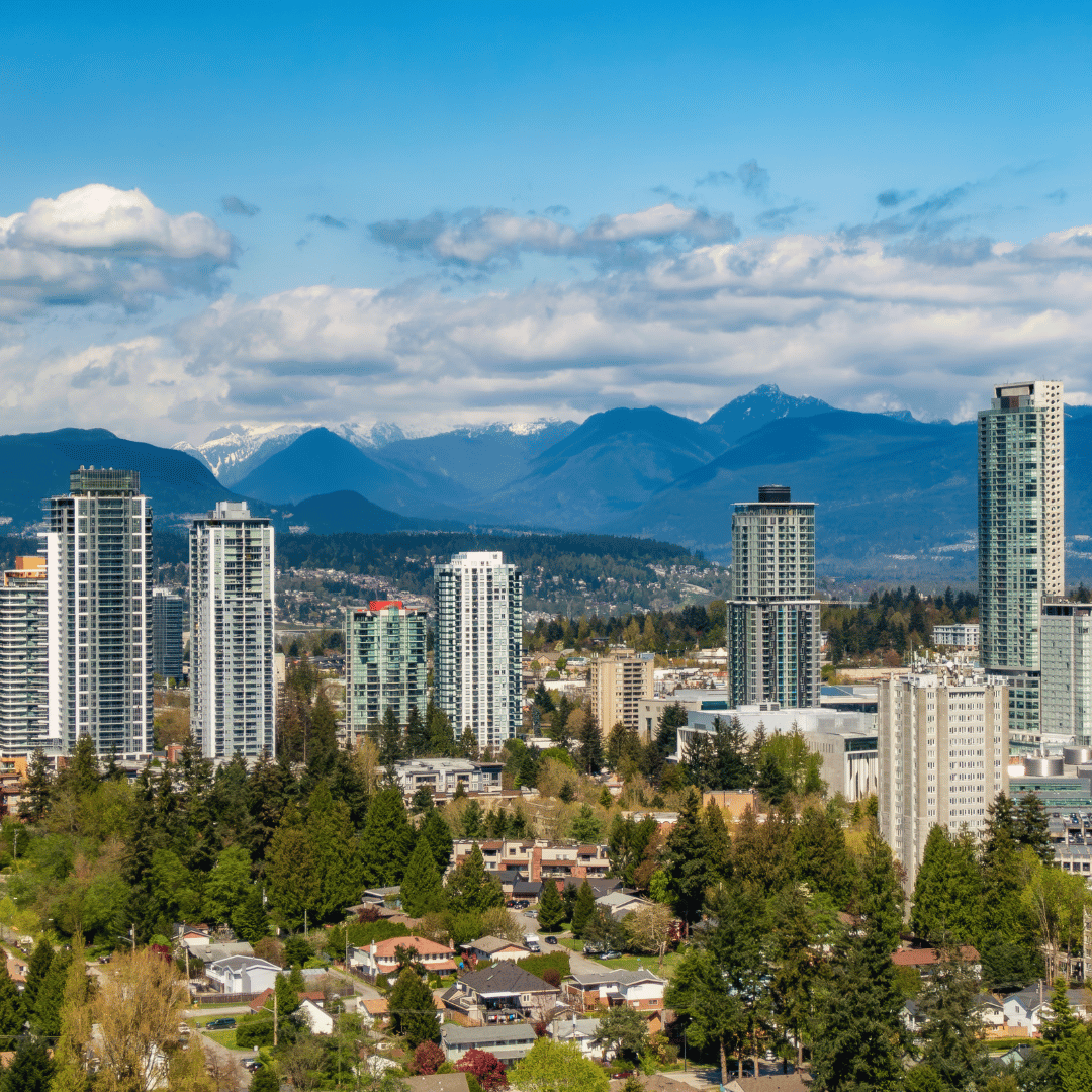 Modern high-rise apartment towers overlook a suburban residential area with tree-lined streets beneath distant mountains.
