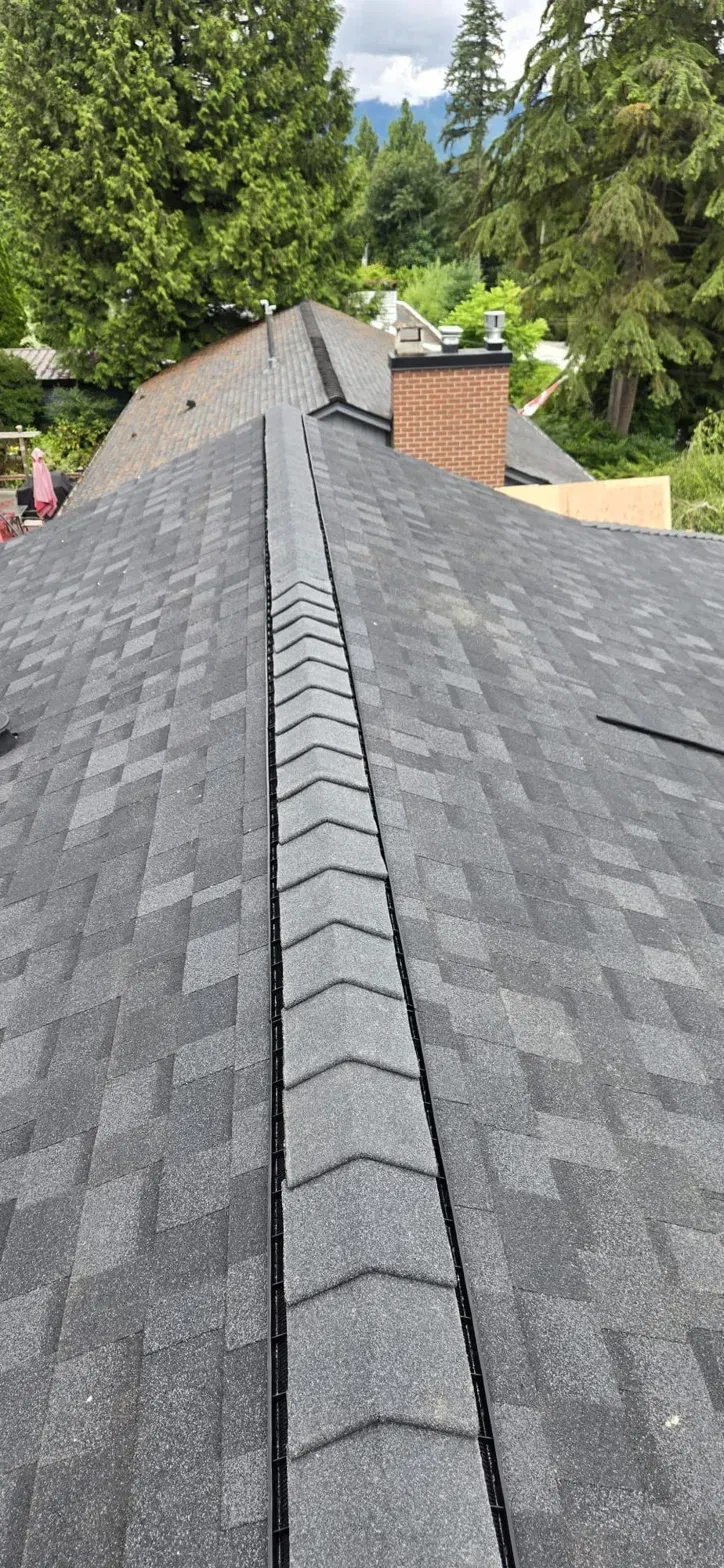 Finished IKO UltraHP ridge caps with brick chimney and Coquitlam mountain backdrop on Thermal Drive, Paragon Roofing BC