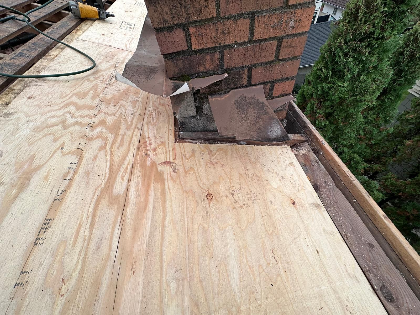 A piece of wood is sitting on top of a roof next to a brick chimney.