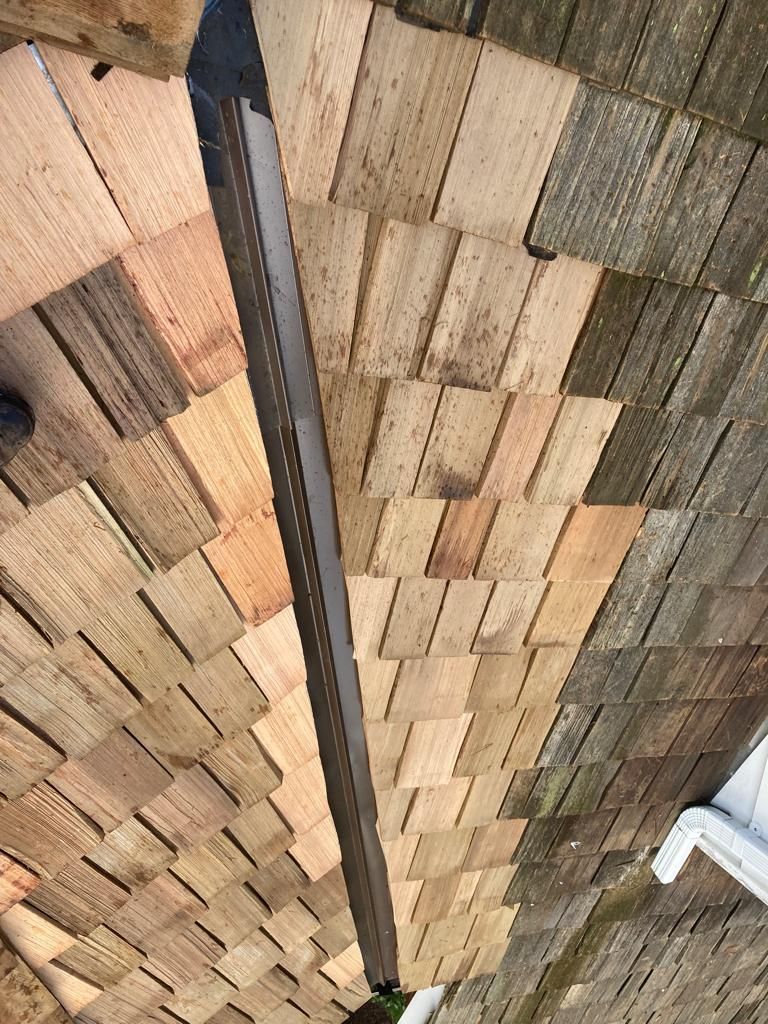 A metal hip cap or ridge vent strip installed vertically over new wooden roof shingles.