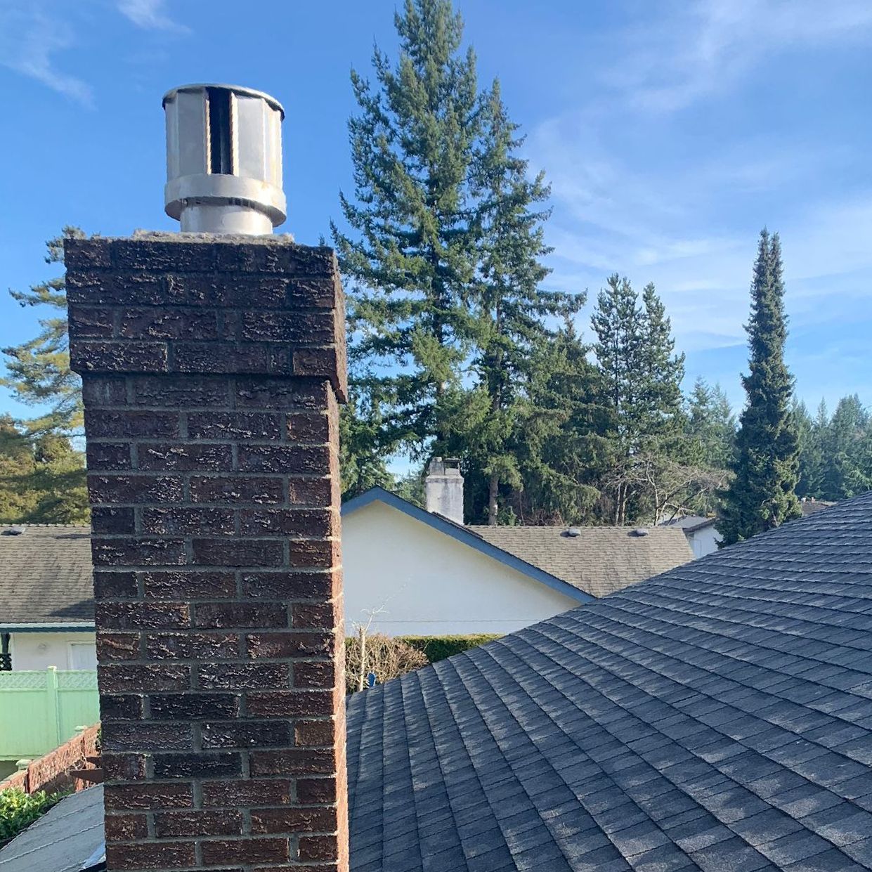 A brick chimney on top of a roof with trees in the background