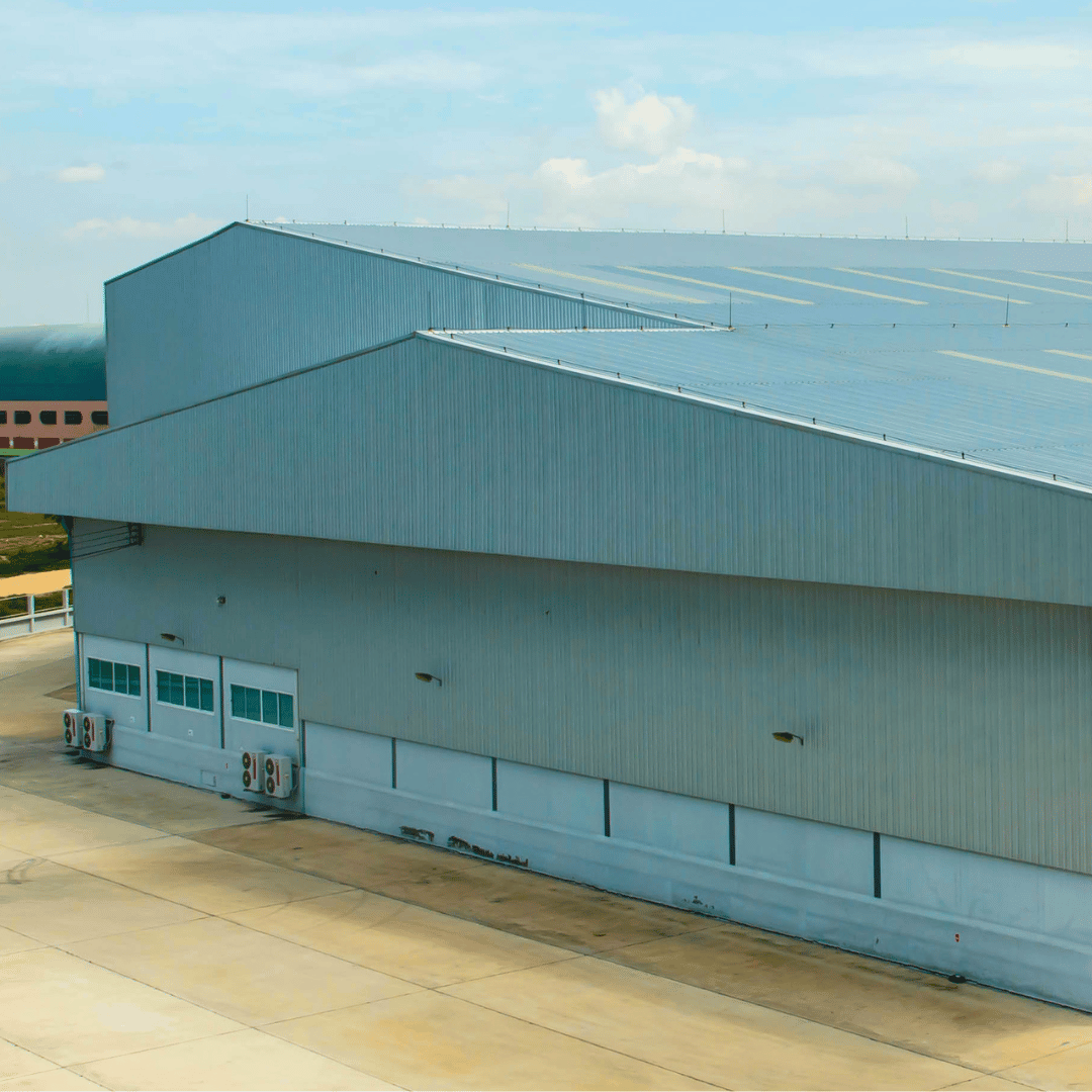 A gray, metal-sided warehouse building with a gabled roof, viewed from an elevated angle above a paved lot.