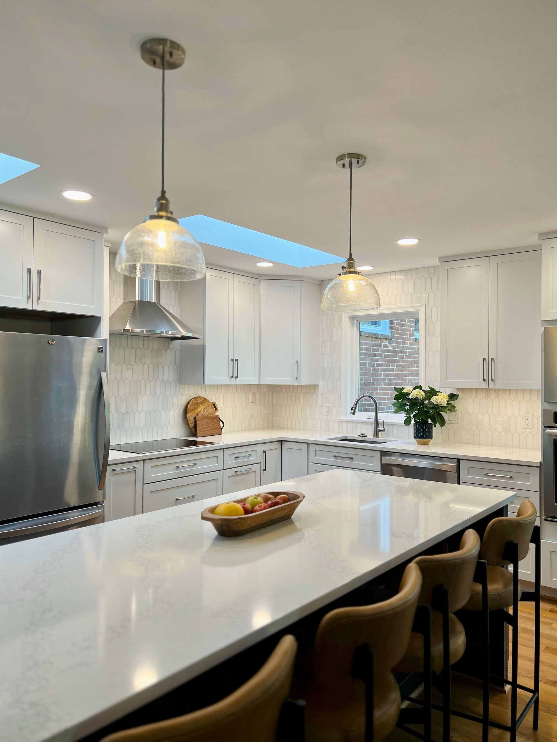 Bright white modern kitchen with island, pendant lights, stainless fridge, and a bowl of fruit on the counter in Rockville