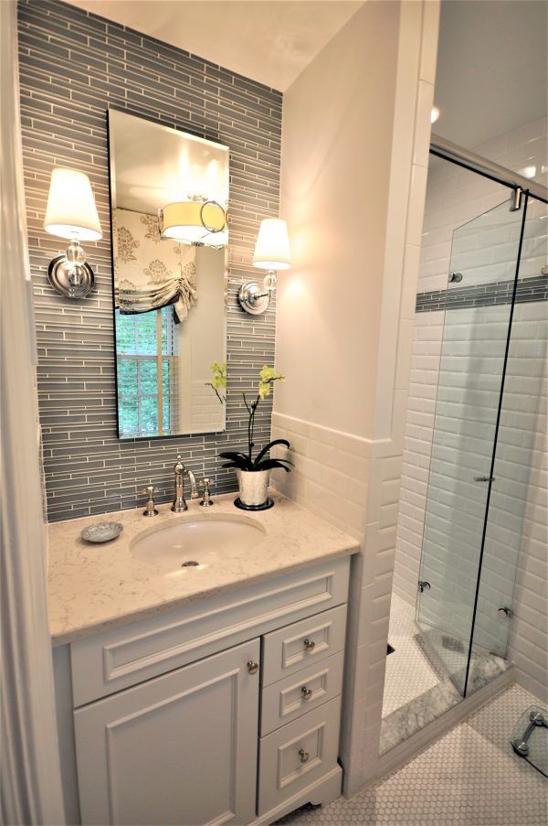 Small bathroom vanity with mirror and sconces beside a glass shower with white subway tile.in Rockville