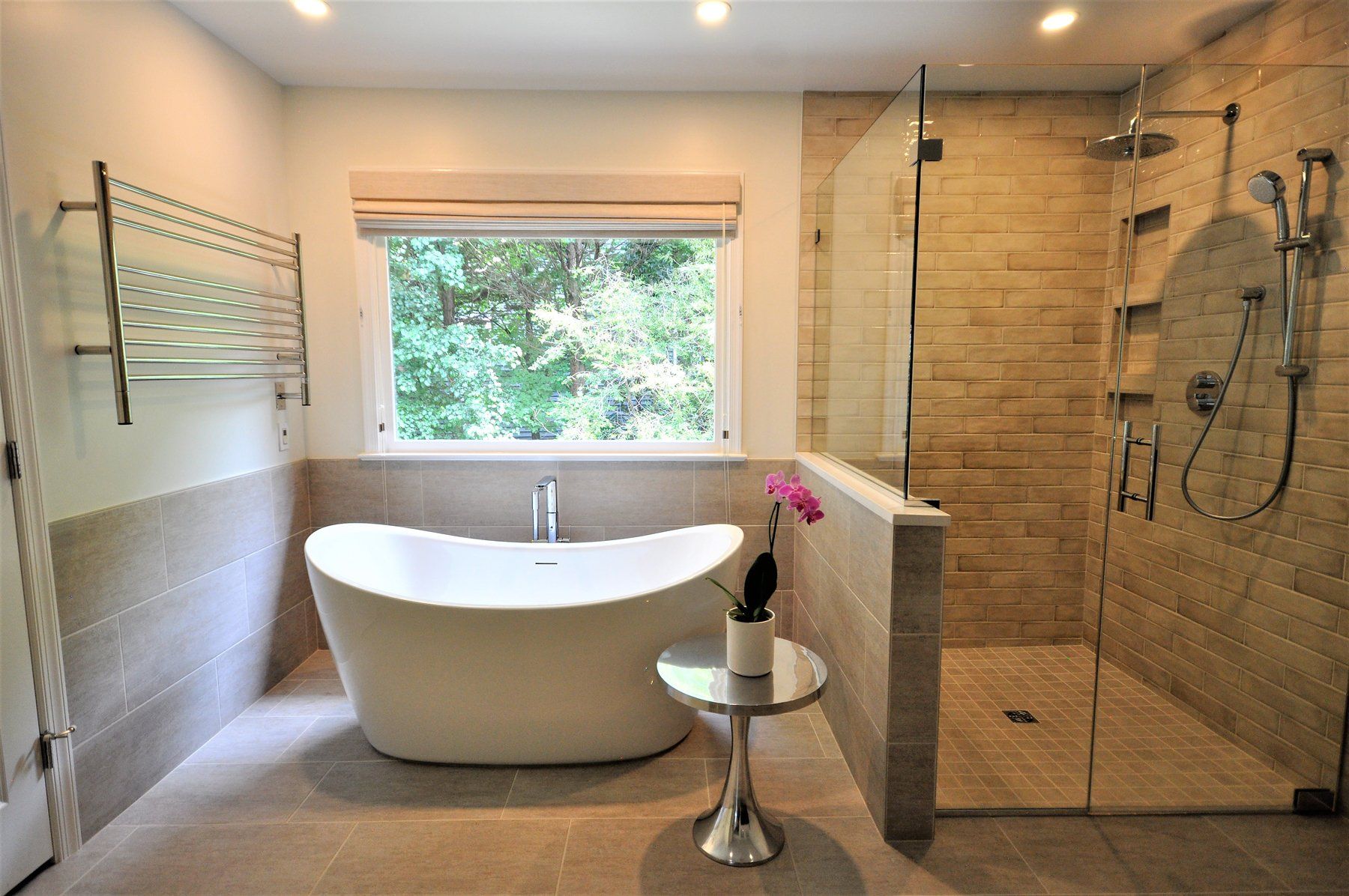 Modern bathroom with freestanding tub, glass shower, and large window overlooking greenery in Gaithersburg