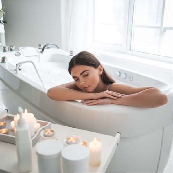 Woman resting in a white bathtub with lit candles in a bright bathroom in Rockville
