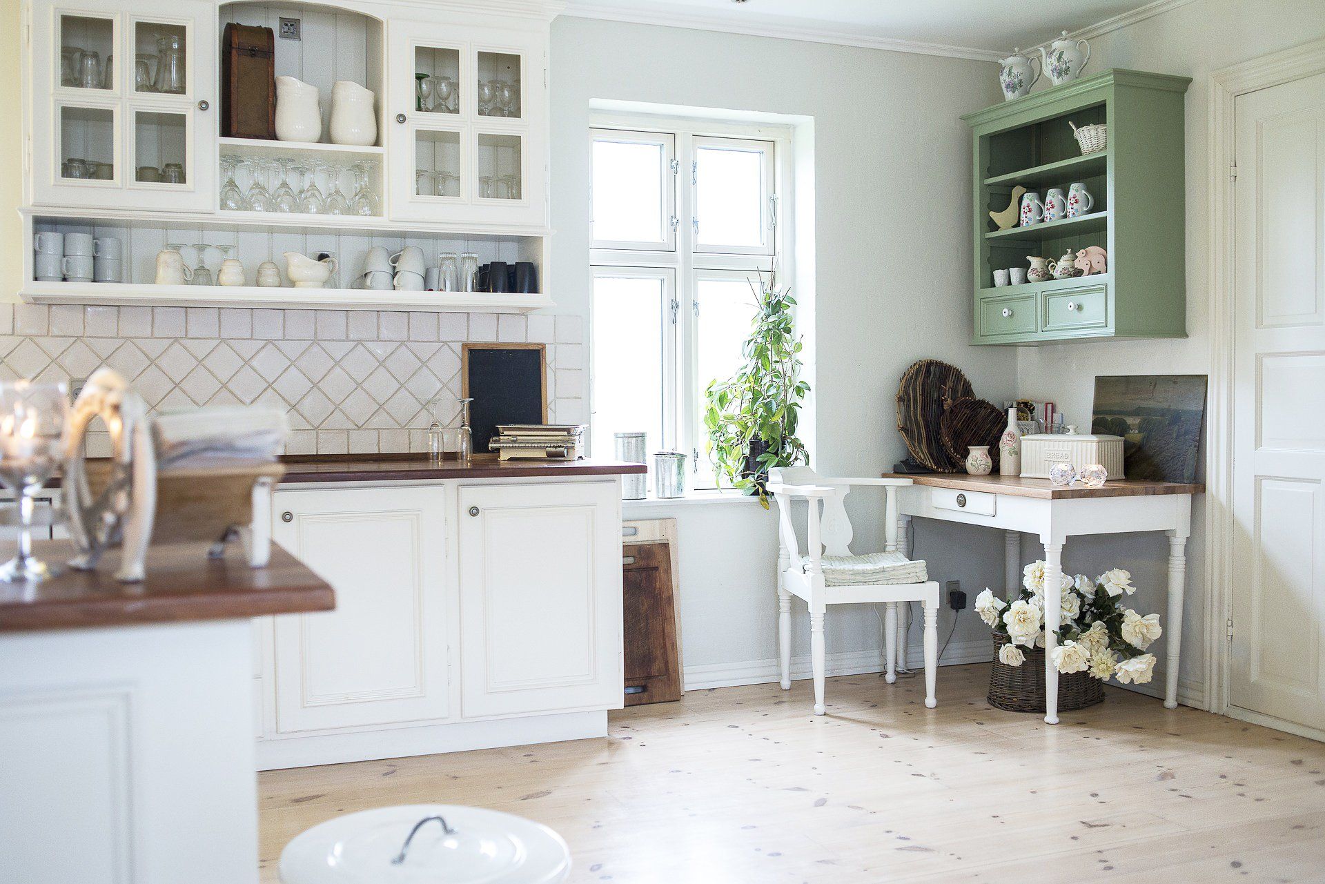 Bright white kitchen and dining nook with pale green cabinets, a table, chairs, and a large window  in Rockville