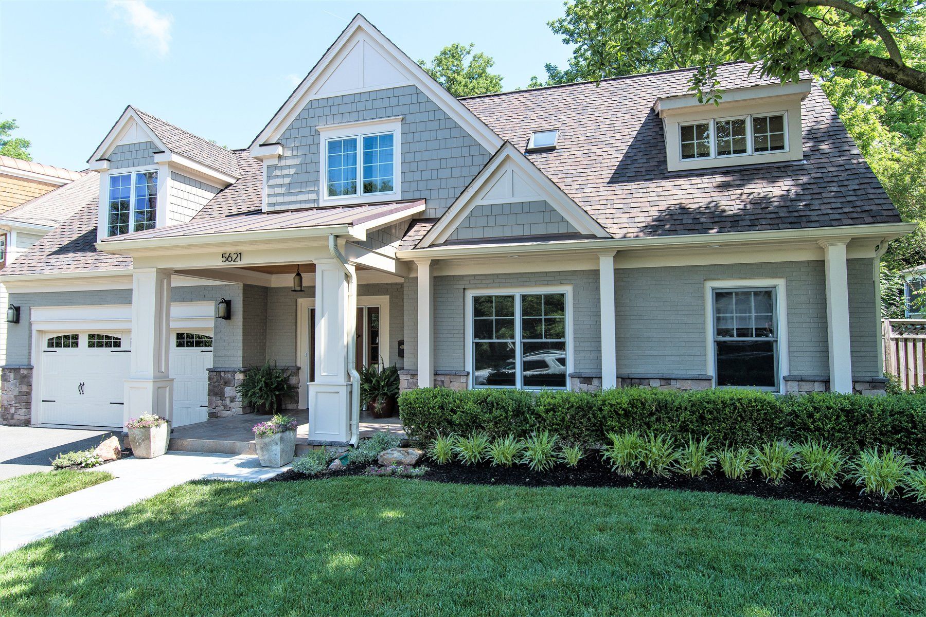 Suburban house with gray roof, white trim, front porch, garage, and green lawn in Rockville