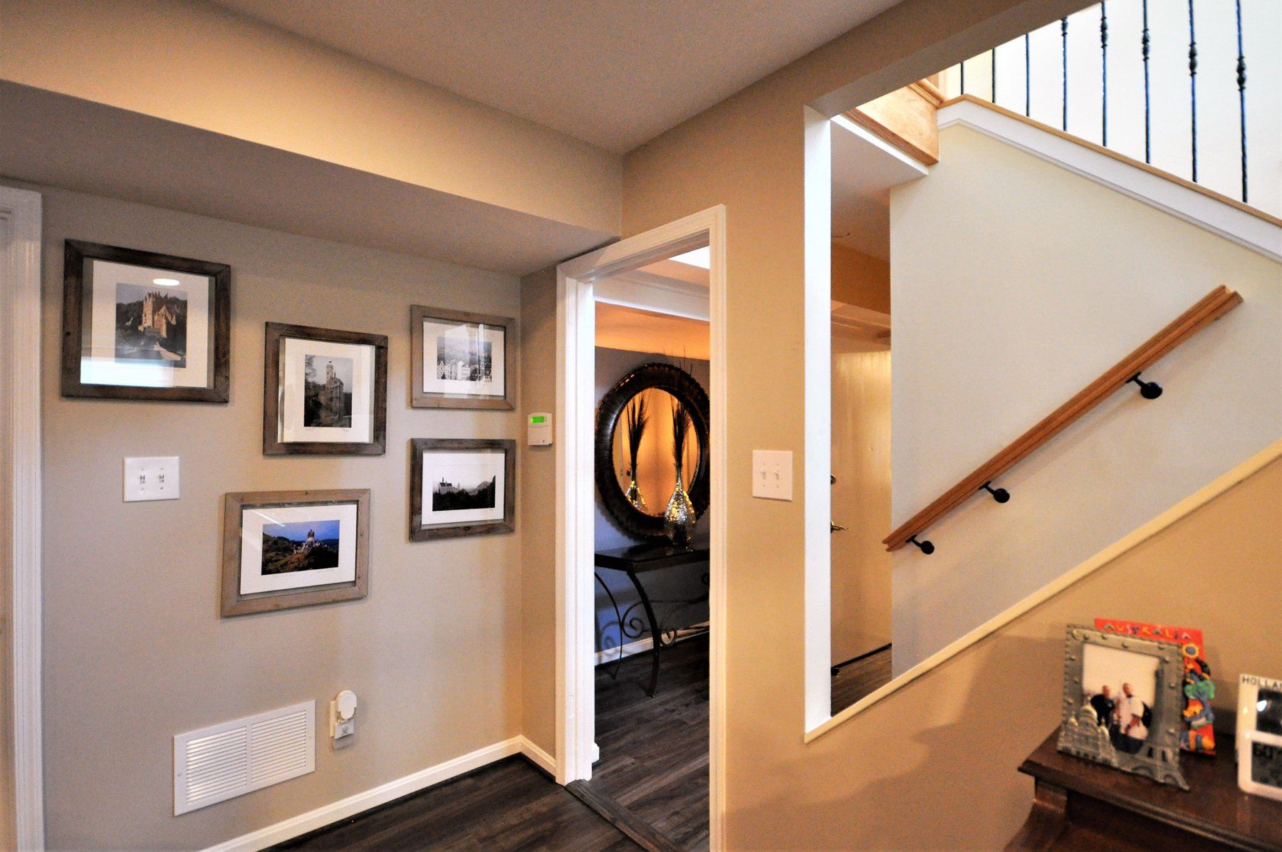 Hallway with framed photos on a beige wall, open doorway, and staircase with wooden handrail in Rockville