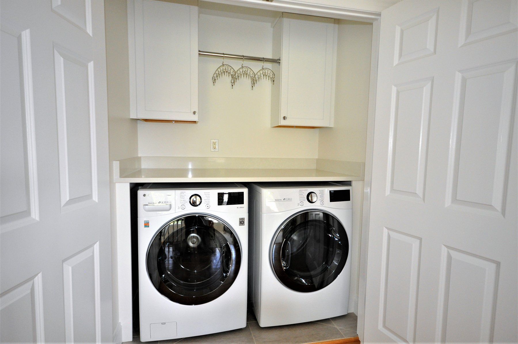Laundry closet with stacked front-loading  washer and dryer under white cabinets in Rockville