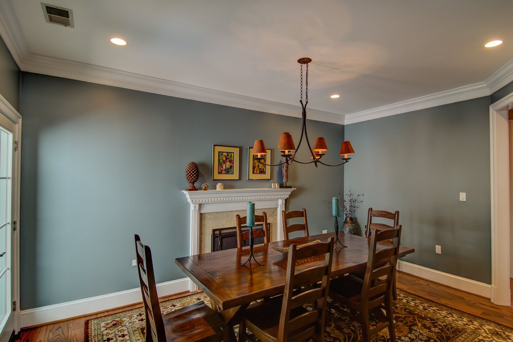 Dining room with gray walls, wooden table and chairs, chandelier, and white fireplace mantel in Rockville