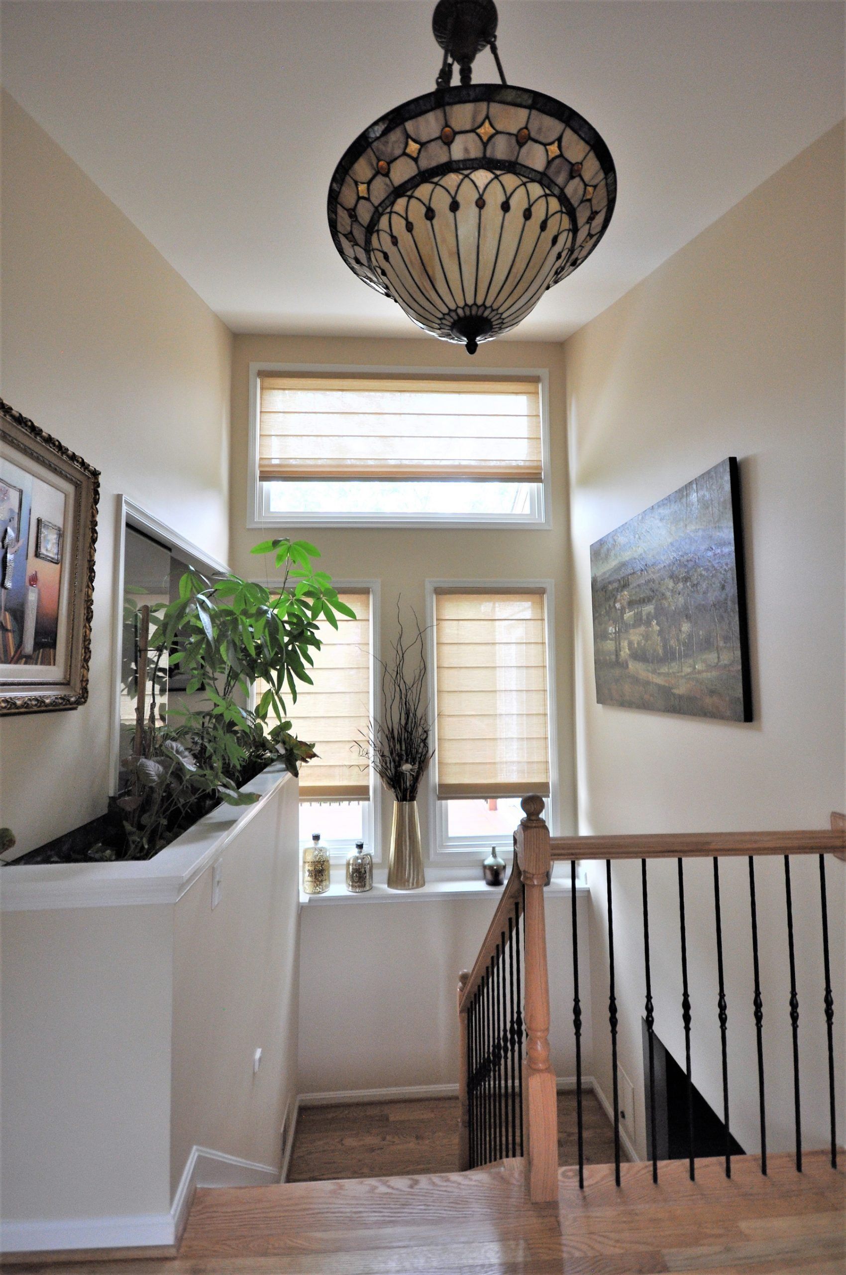 Stair landing with chandelier, potted plant, framed art, and window overlooking a bright hallway in Rockville