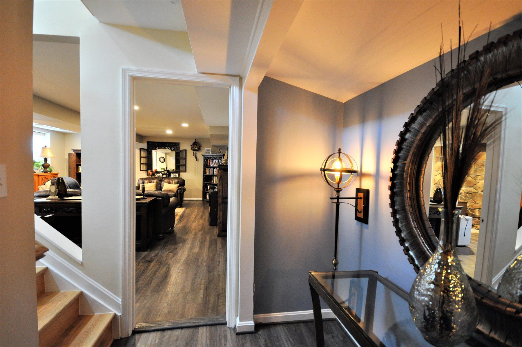 Modern hallway with mirror, wall sconce, and decorative vase, opening into a dining room with wood floors in Rockville