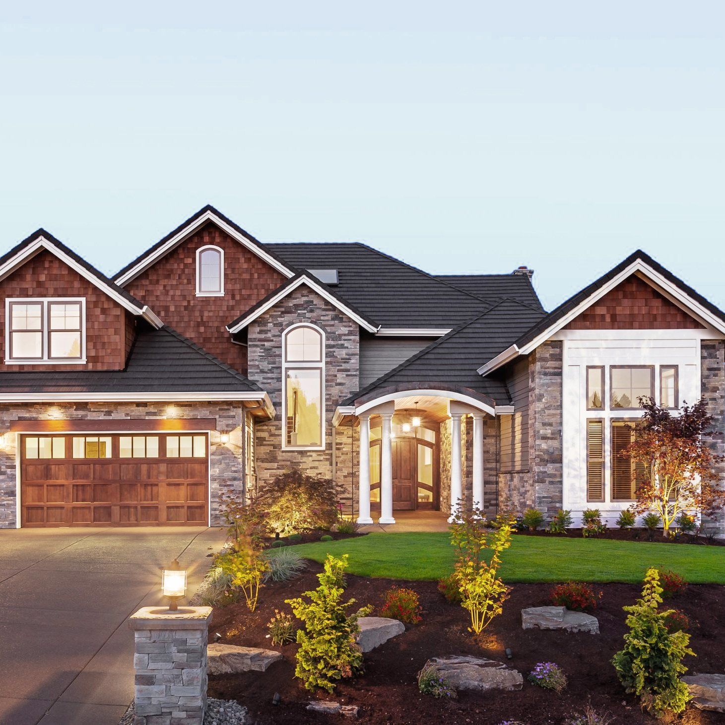 Luxury suburban house with stone and brick facade, lit entryway, and landscaped front yard at dusk in Rockville