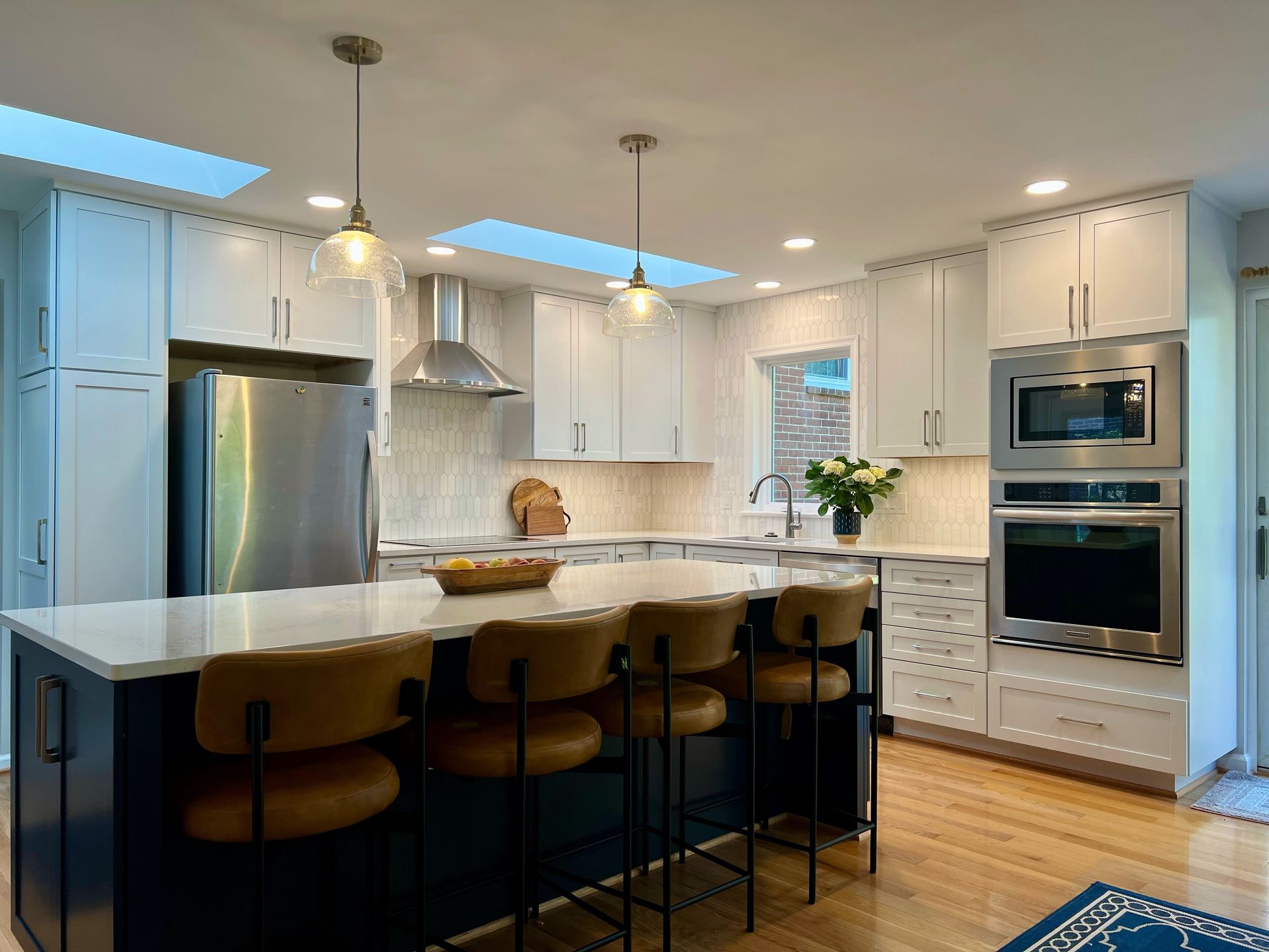 Modern white kitchen with island, bar stools, stainless appliances, and wood floors in Rockville