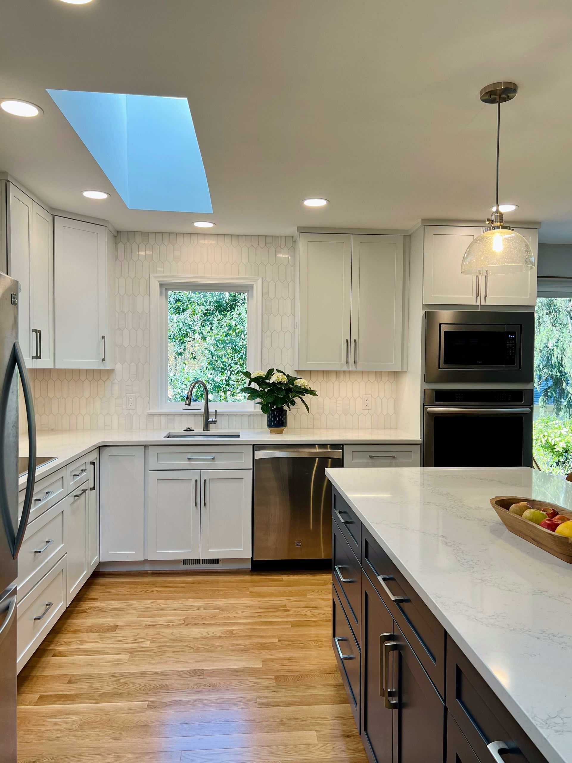 Bright white kitchen with island, stainless appliances, skylight, and wood floor in Rockville