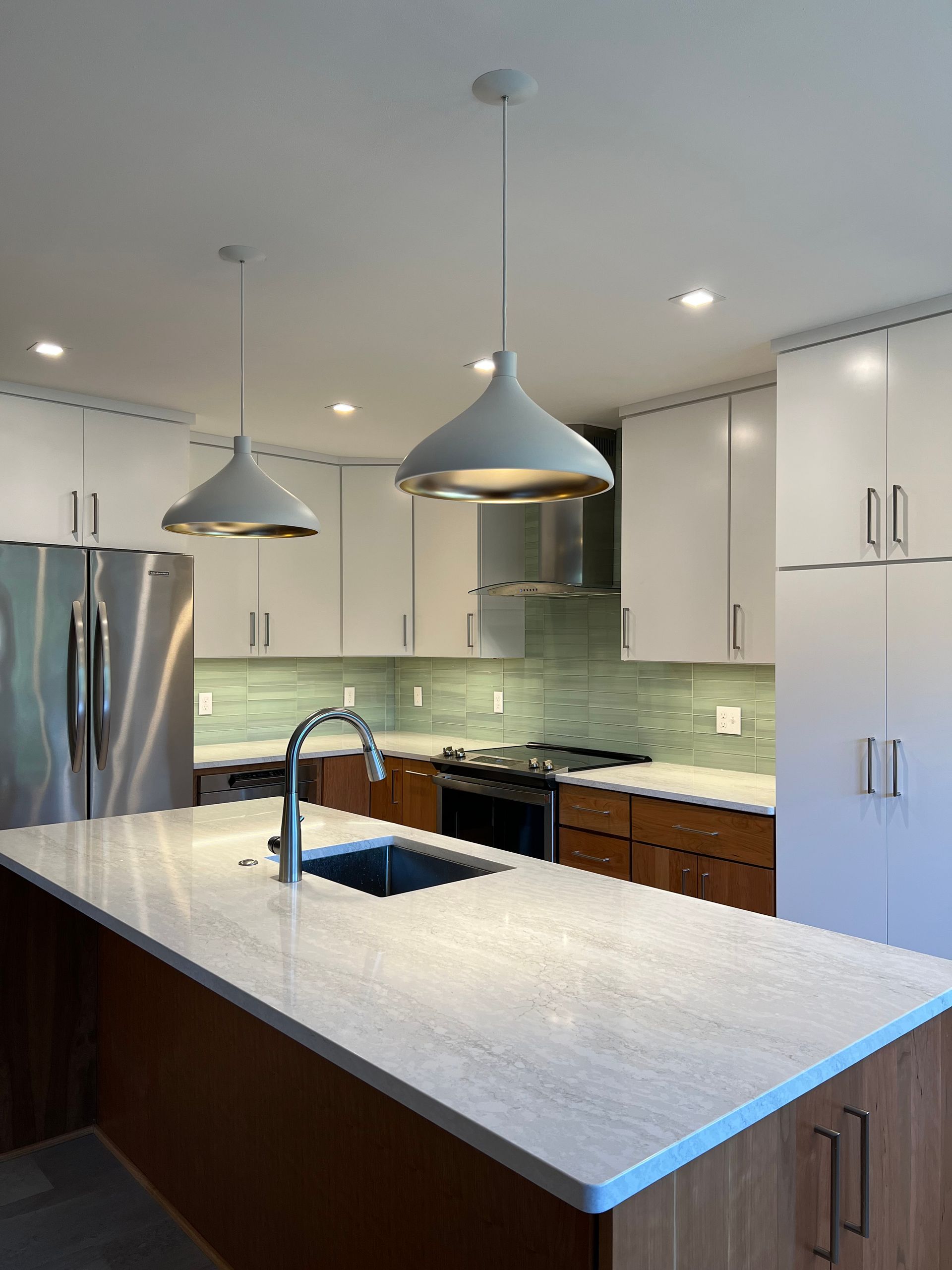 Modern kitchen with stainless steel appliances, white cabinets, large island, pendant lights, and green tile backsplash in Rockville