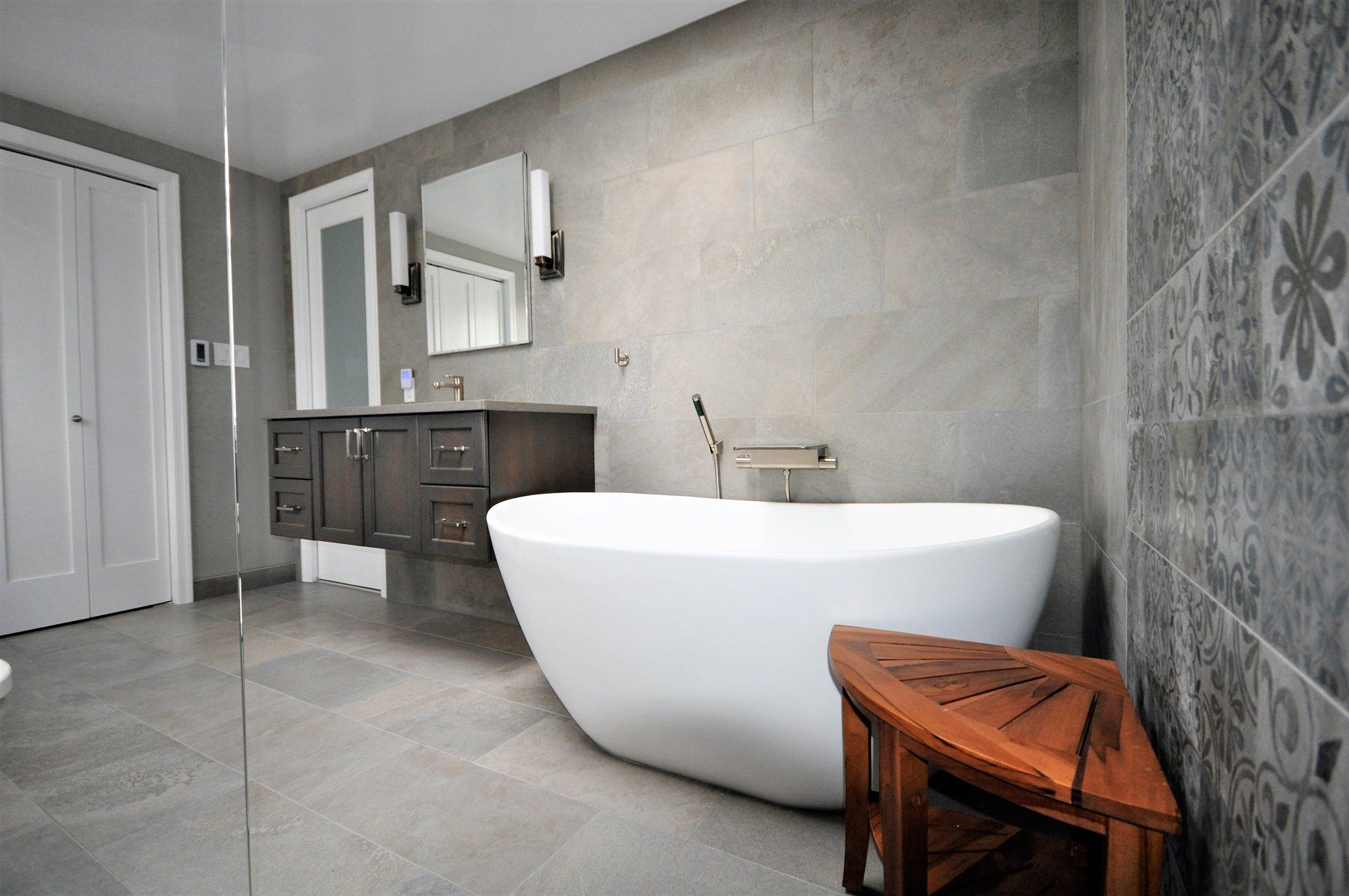Modern gray bathroom with freestanding white tub, dark vanity, and decorative stool  in Rockville