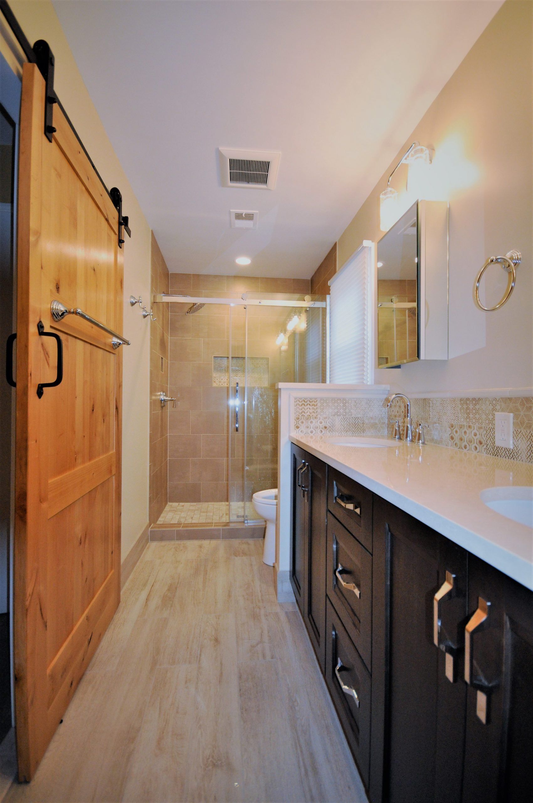 Narrow bathroom with wooden barn door, glass shower, dark vanity, and mirrored countertop  in Rockville