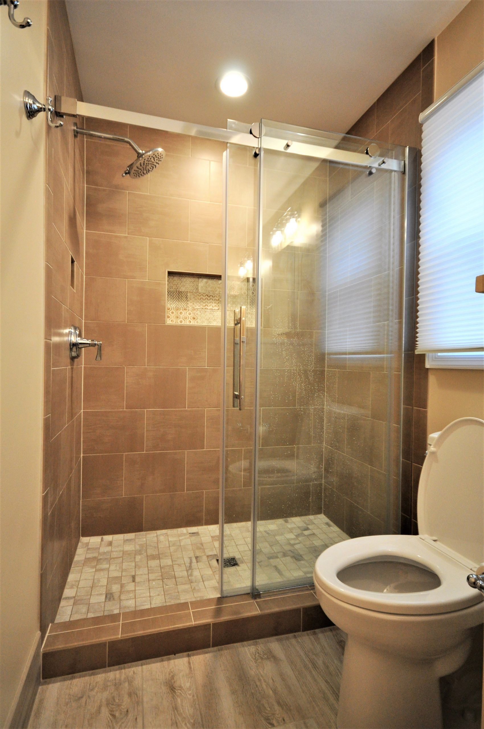 Glass shower stall and toilet in a beige-tiled bathroom with a window  in Rockville