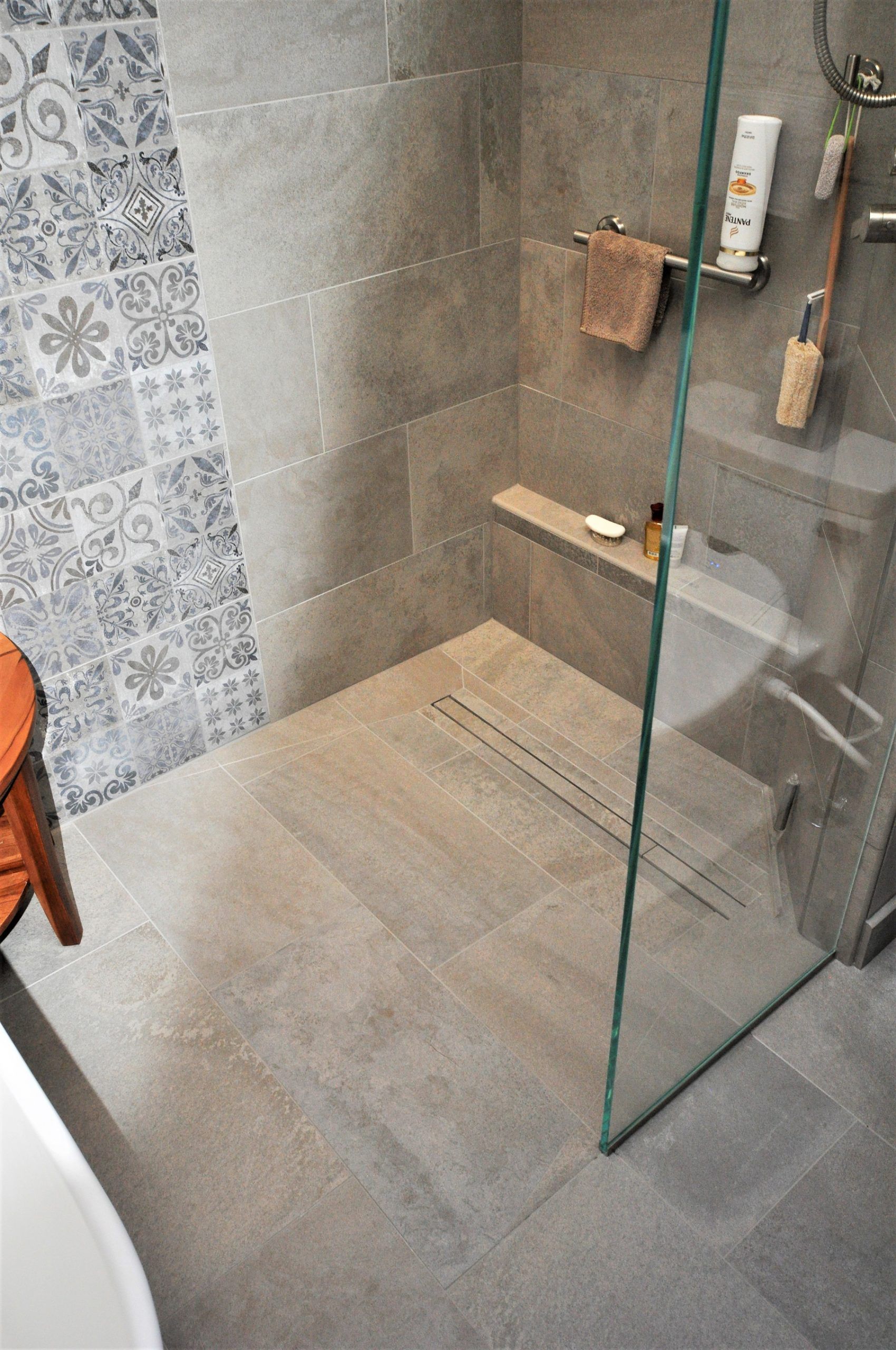 Modern shower stall with gray tile, glass panel, built-in shelf, and bath accessories  in Rockville
