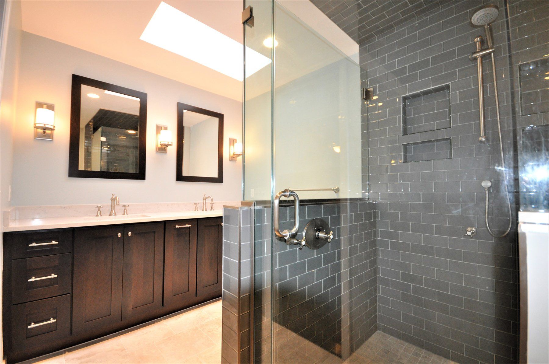 Modern bathroom with dark vanity, mirrors, and a glass-enclosed tiled shower  in Rockville