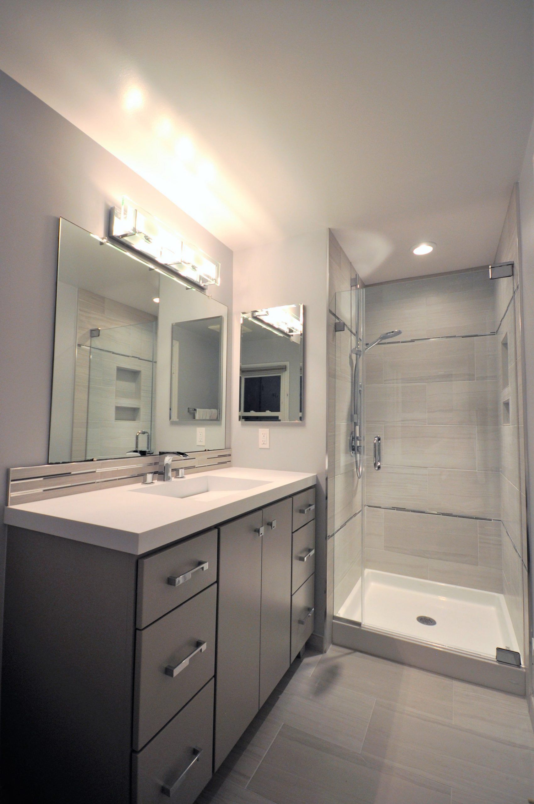 Modern bathroom with vanity, mirror, and glass-enclosed shower in gray and white  in Rockville