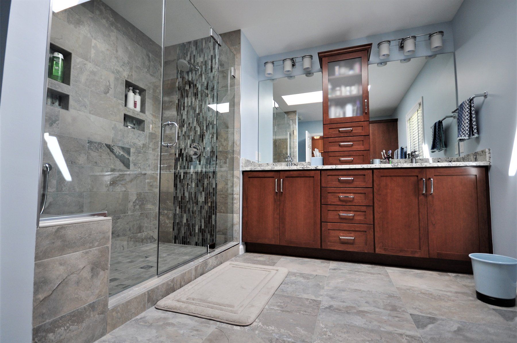 Modern bathroom with gray marble shower, double wooden vanity, and light tile floor in Rockville