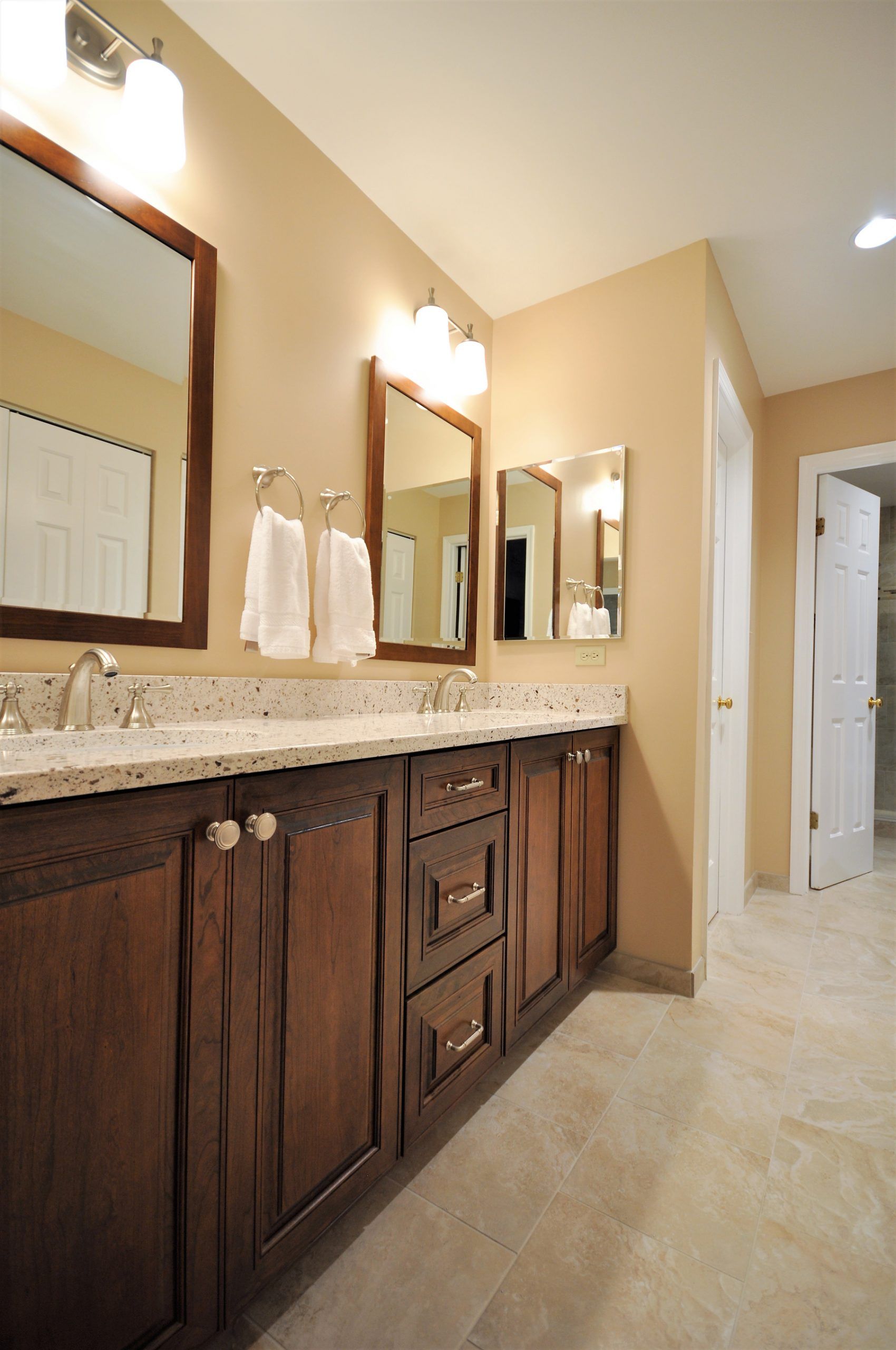 Modern bathroom vanity with dark wood cabinets, granite countertop, mirrors, and wall sconces in Rockville