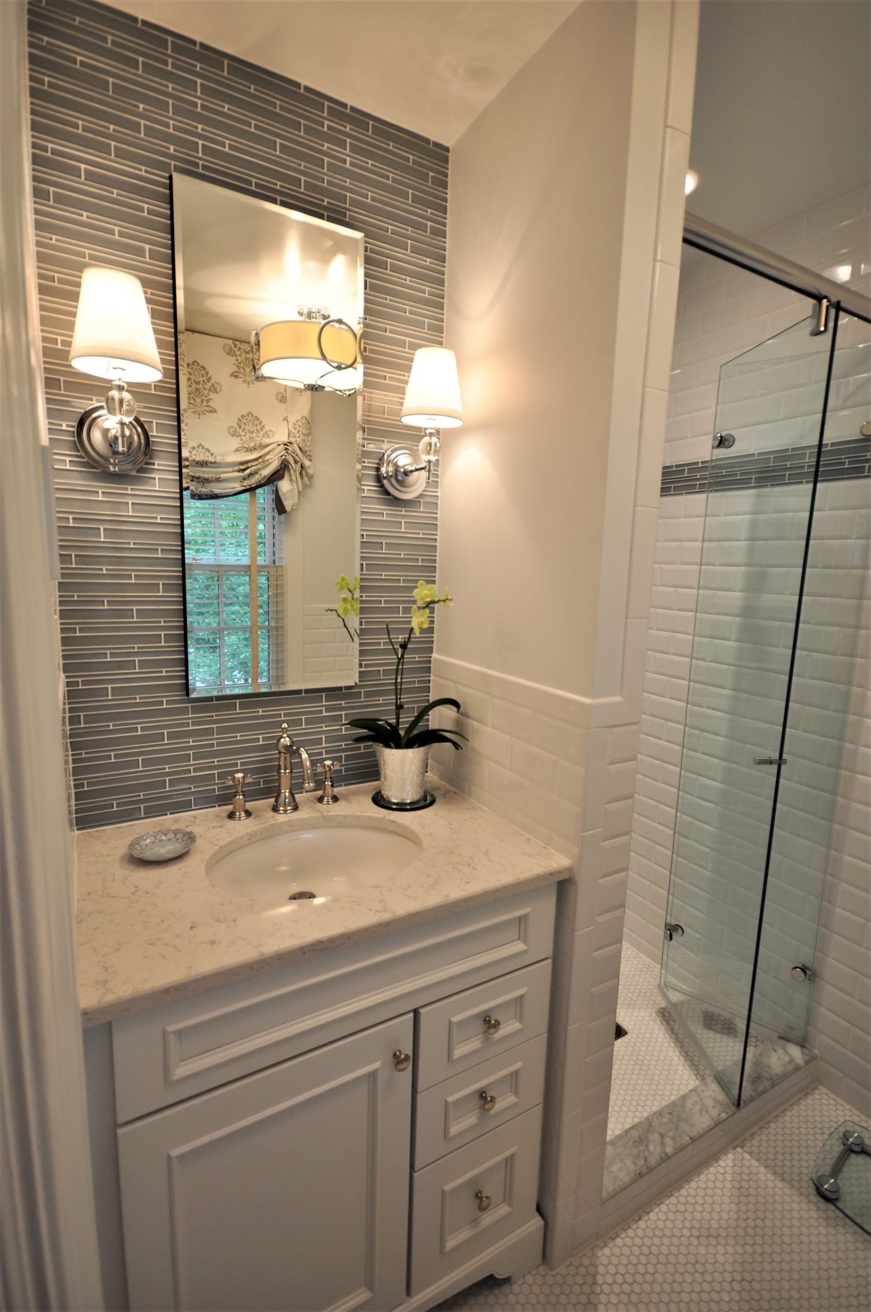 Elegant bathroom vanity with marble counter, mirrored wall sconces, and glass shower enclosure in Rockville