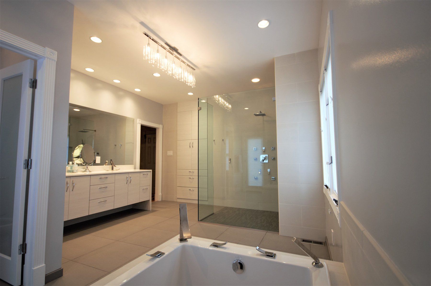 Modern bathroom with double vanity, glass shower, and a large bathtub under recessed lighting in Rockville