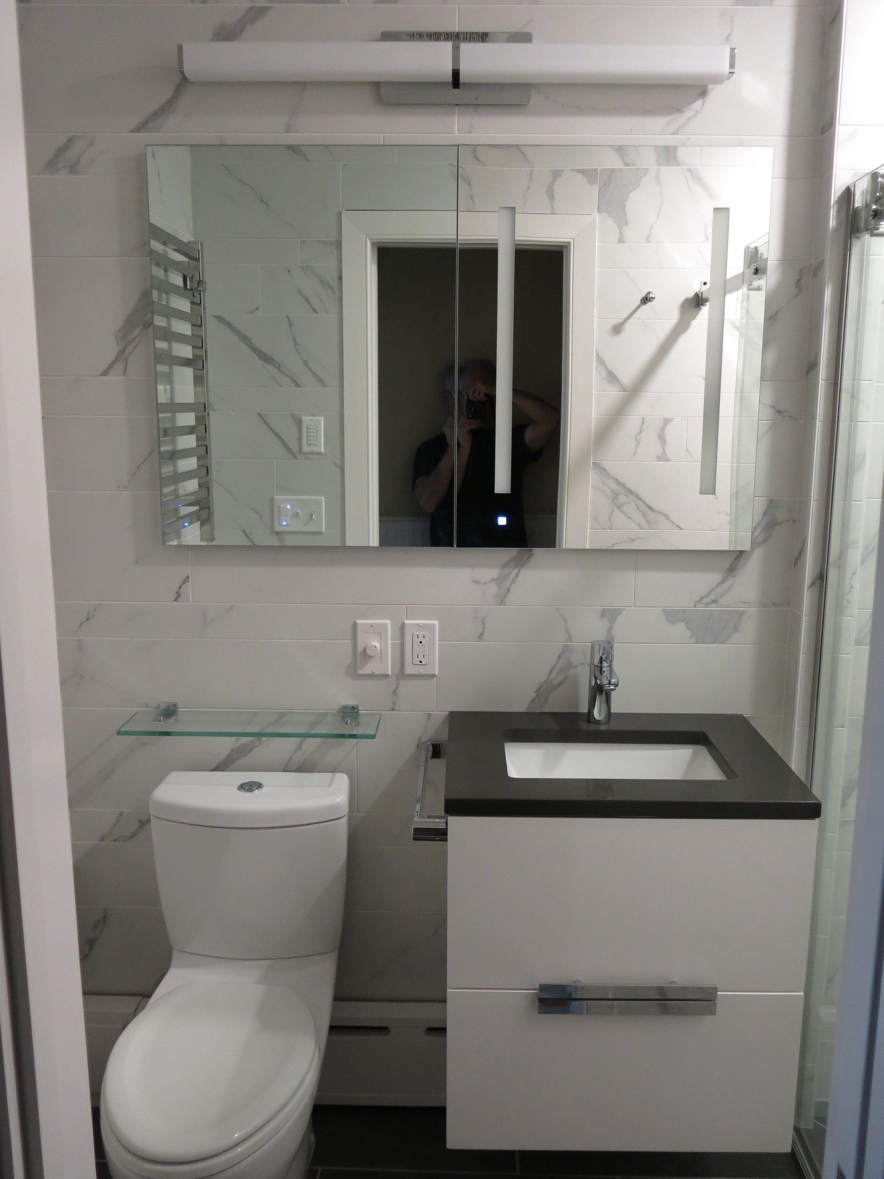 Small modern bathroom with toilet, vanity sink, mirror, and white tiled walls in Montgomery Country MD