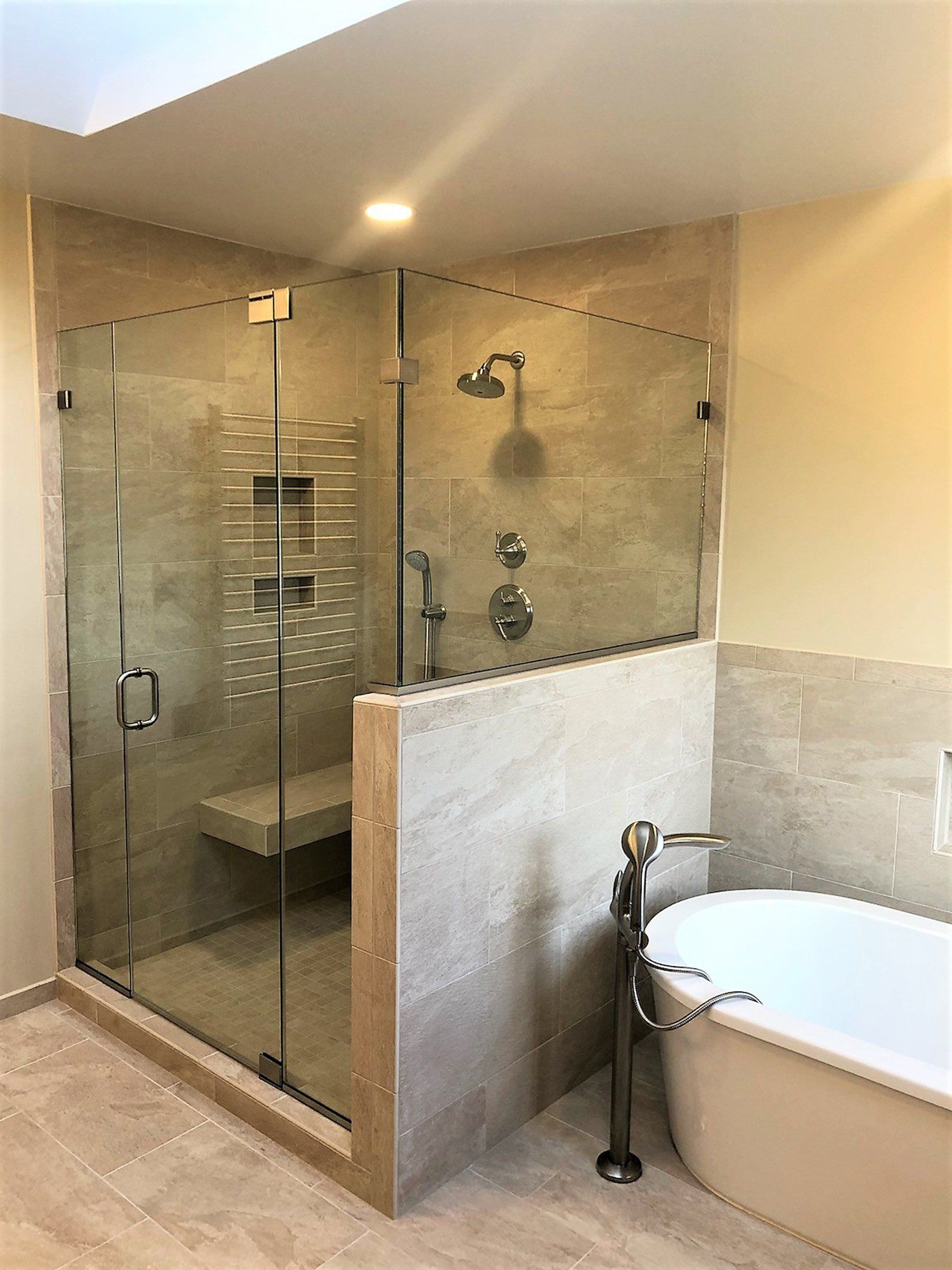 Modern bathroom with glass walk-in shower, beige tile, and a bathtub in the foreground in Rockville